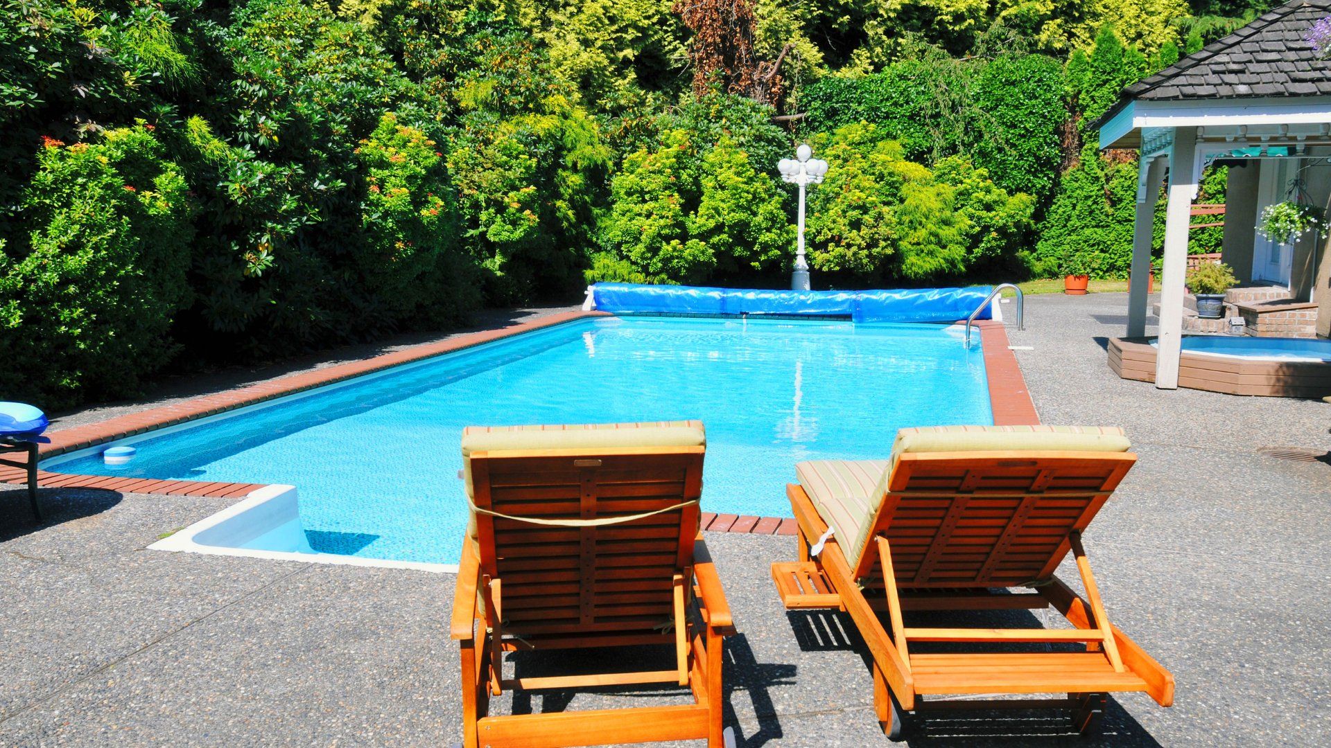 Two patio chairs looking onto a backyard pool. The deck surrounding the pool is concrete.