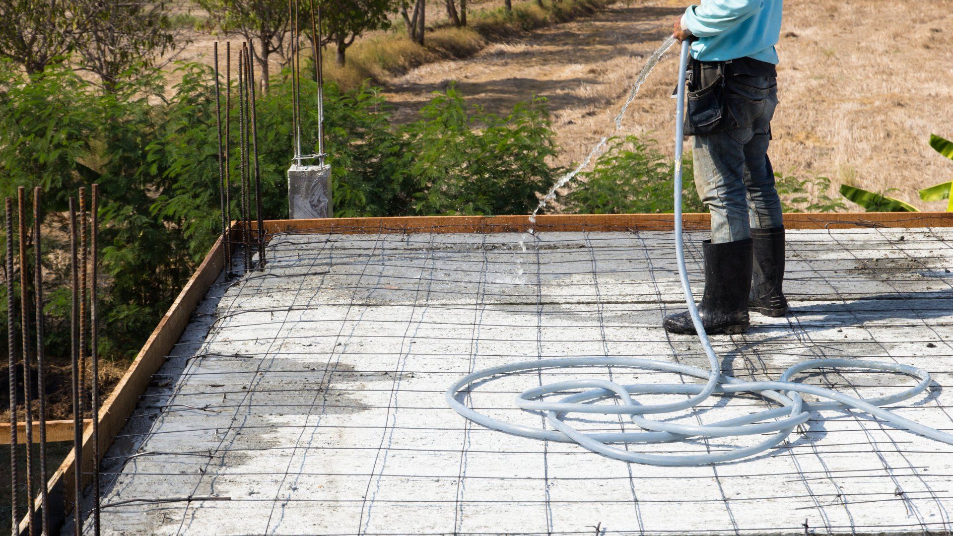 A concrete contractor spraying water on a a slab on grade build in a backyard.