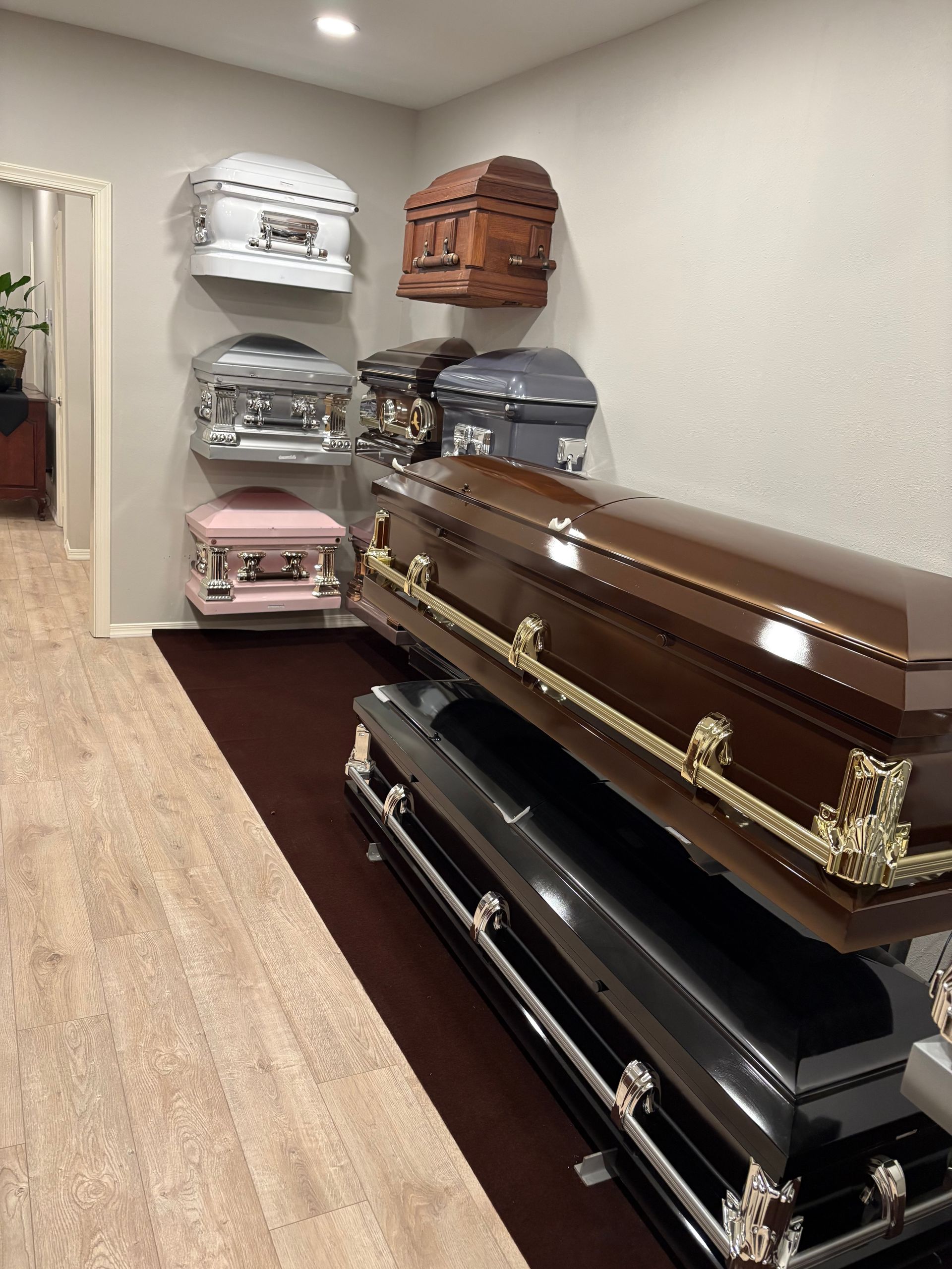 Funeral home display room with several caskets lined up on carpet and a wood floor