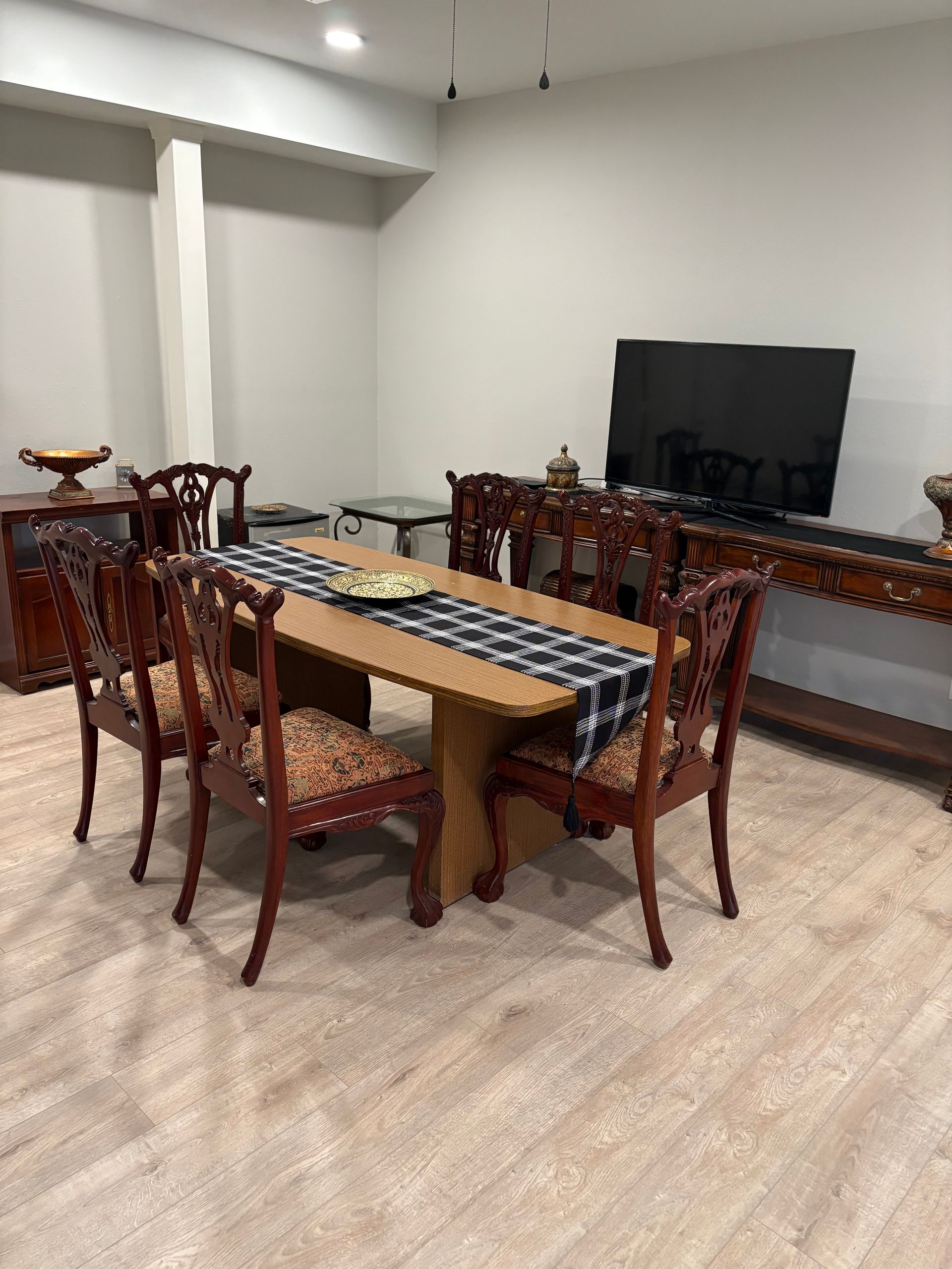 Dining room with a wooden table, patterned chairs, and a TV on a sideboard.