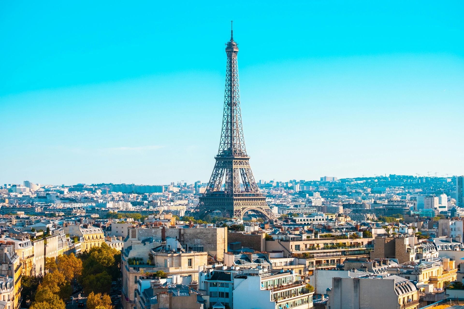 Eiffel Tower towering over Paris cityscape under a bright blue sky.