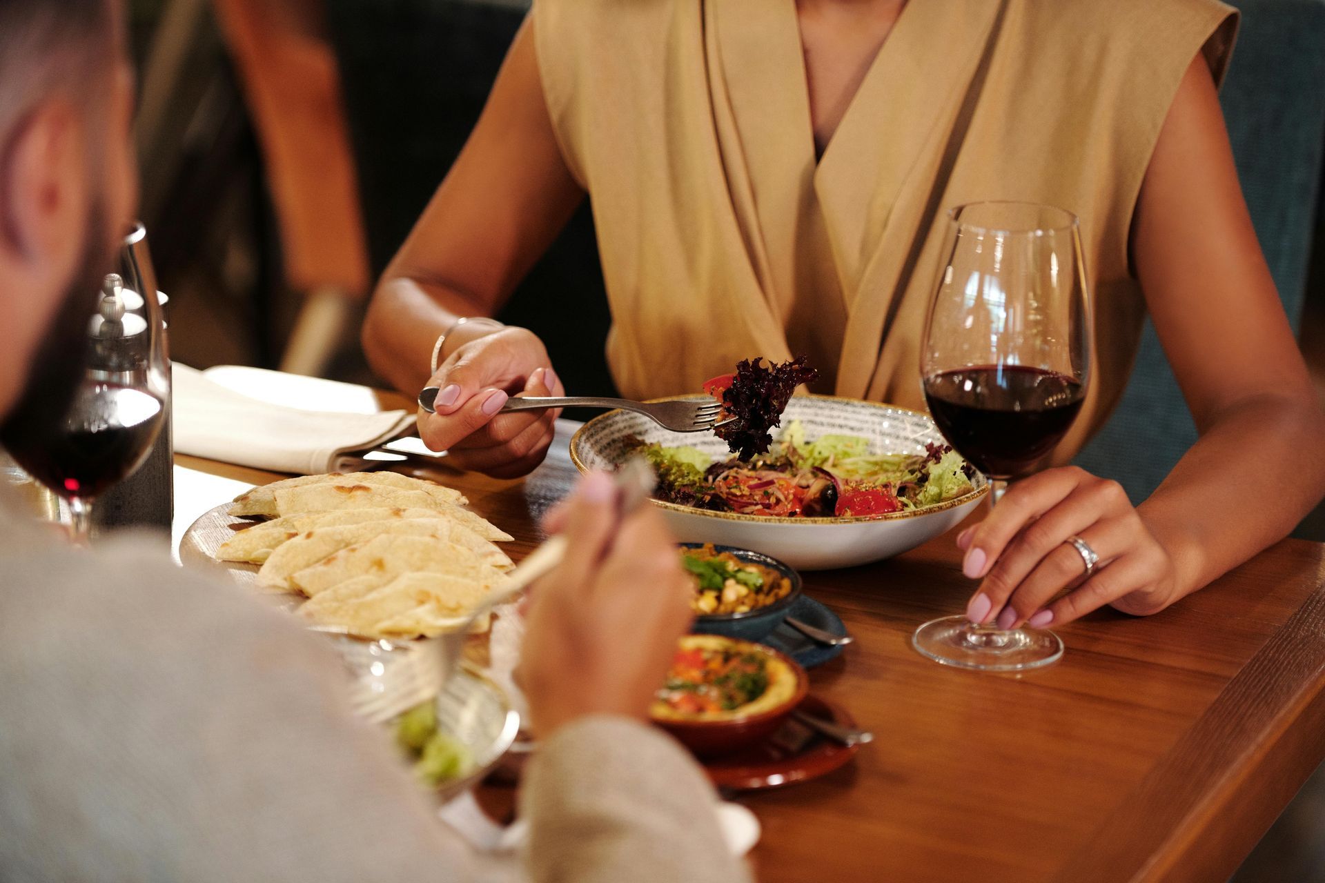 Couple eating salad and appetizers at a restaurant, with red wine glasses on the table.