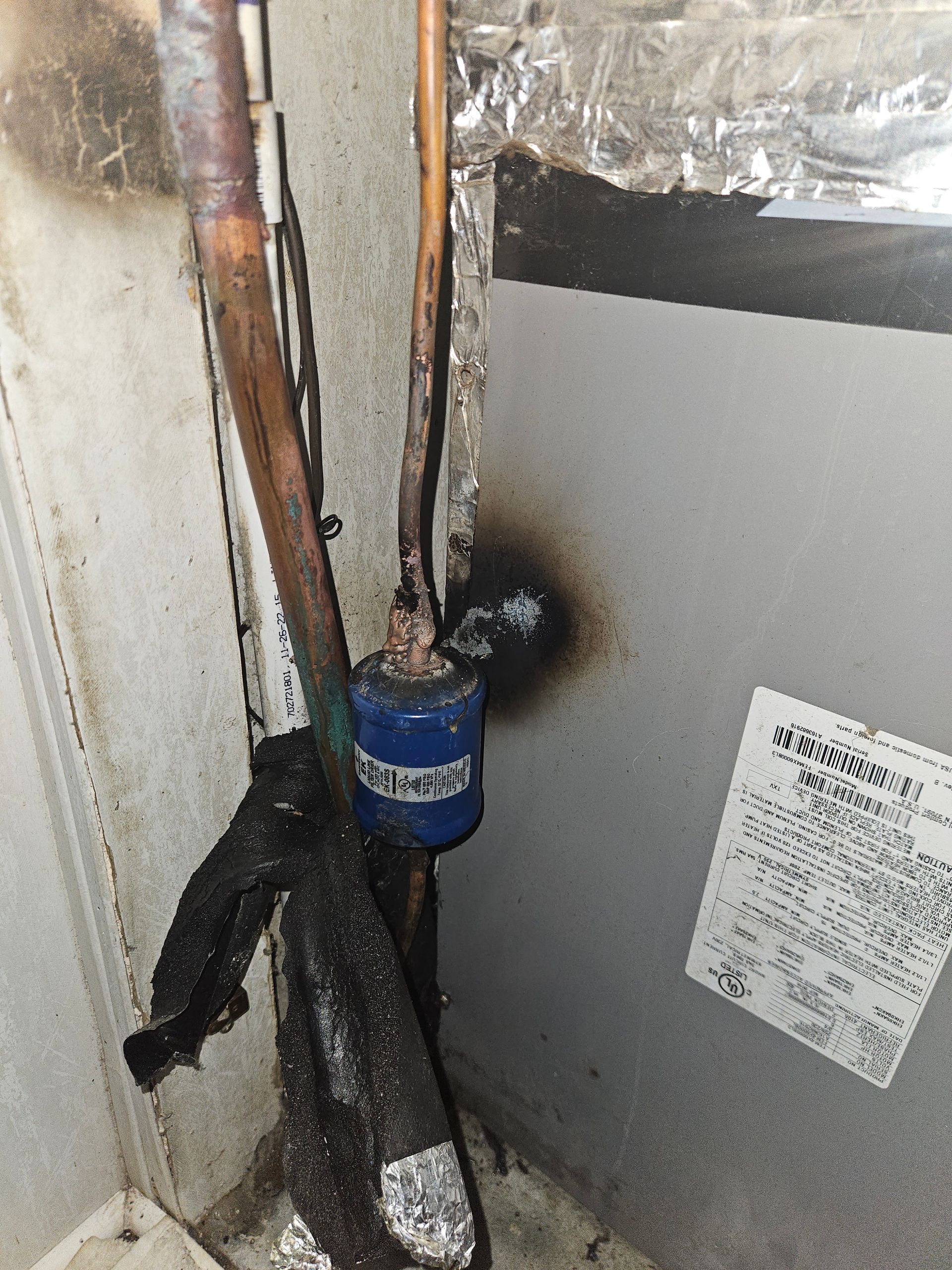 HVAC unit with exposed copper pipes and wrapped insulation in a utility closet