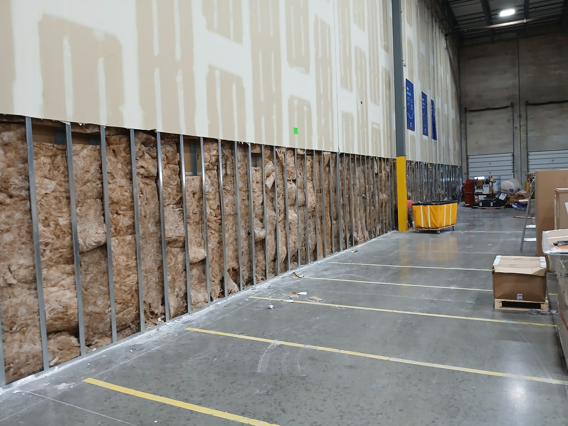 Warehouse aisle with exposed insulation walls, yellow floor lines, and stacked boxes