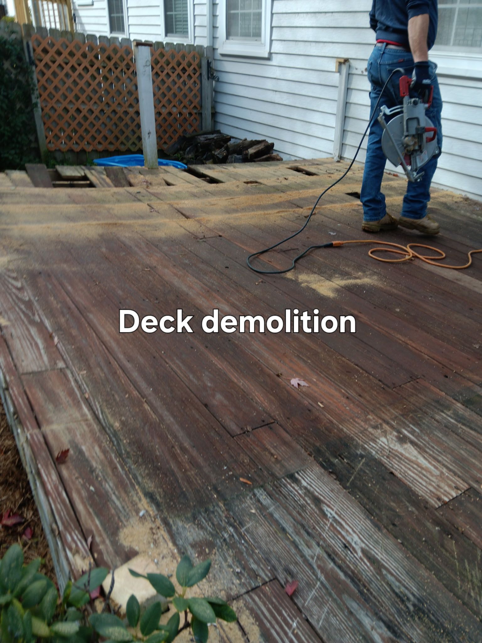 Worker using a jackhammer to remove wooden deck boards in a backyard.