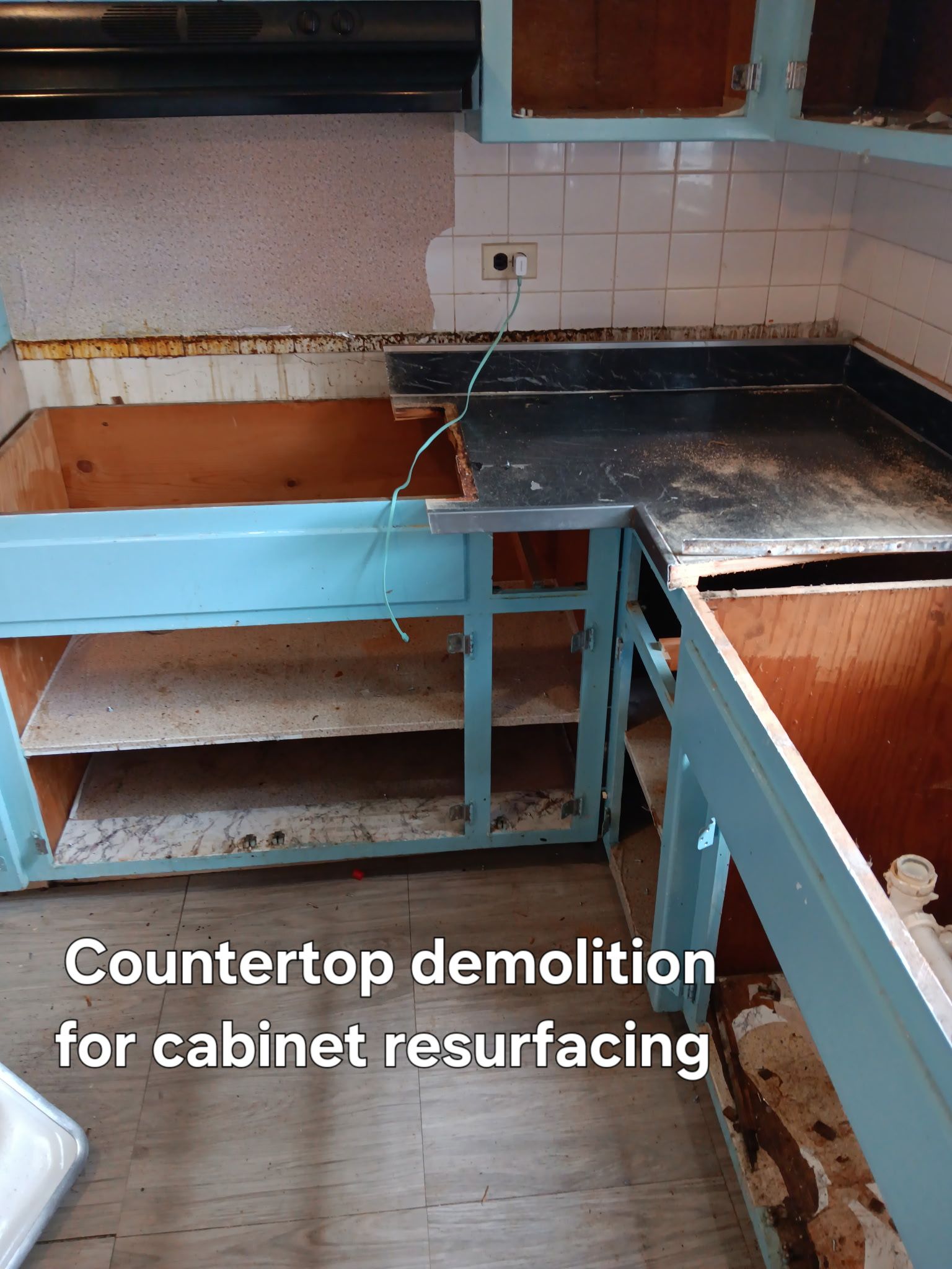 Damaged kitchen counter and cabinets being demolished for resurfacing, with exposed sink and backsplash.