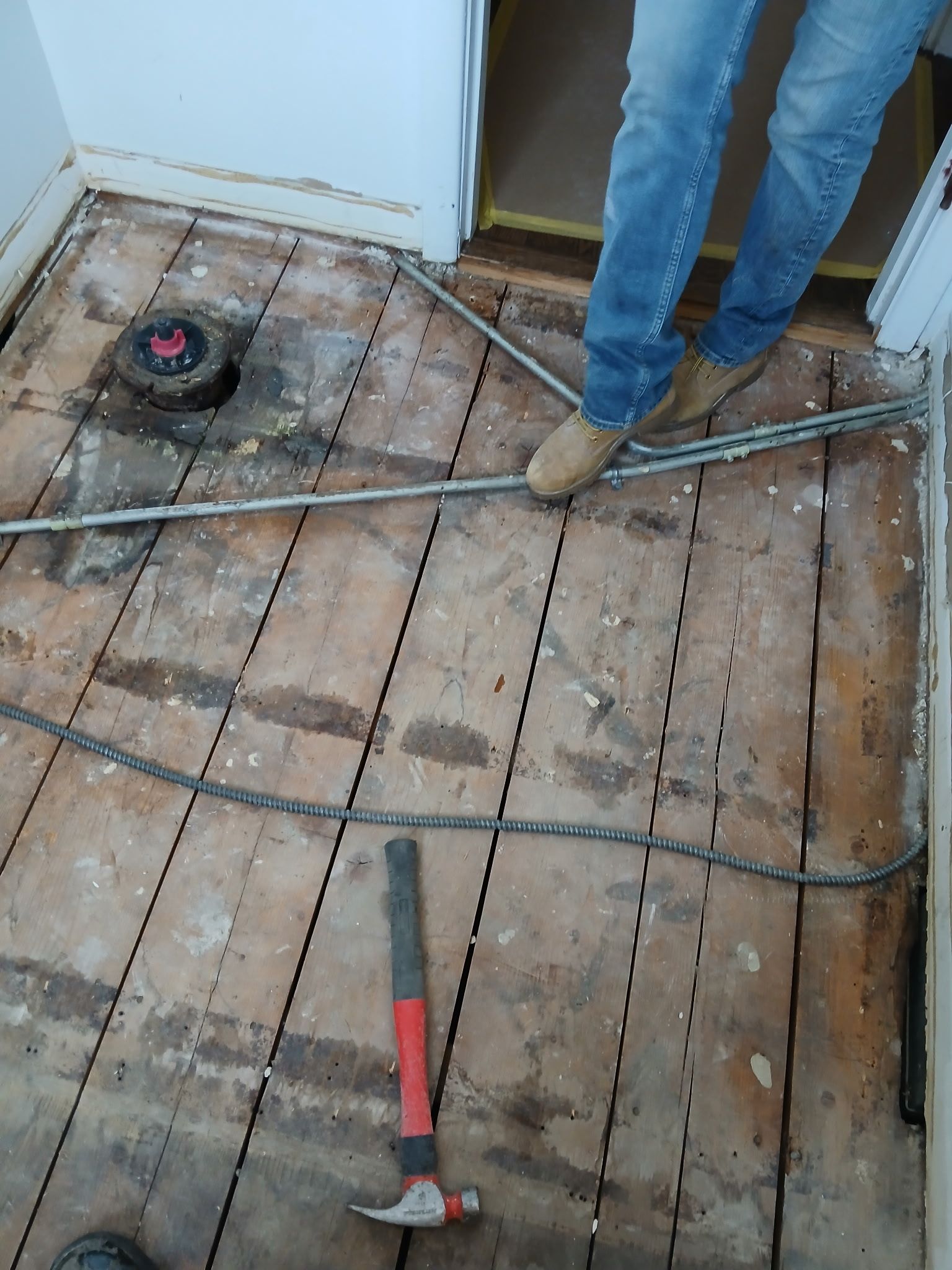 Construction tools on a bare wooden floor, with a person’s legs visible near the doorway.