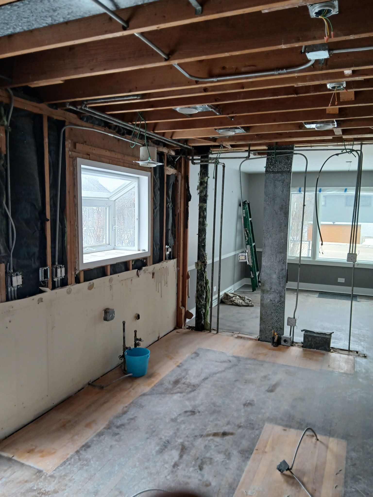 Partially renovated room with exposed ceiling beams, stripped walls, a window, and construction debris on the floor
