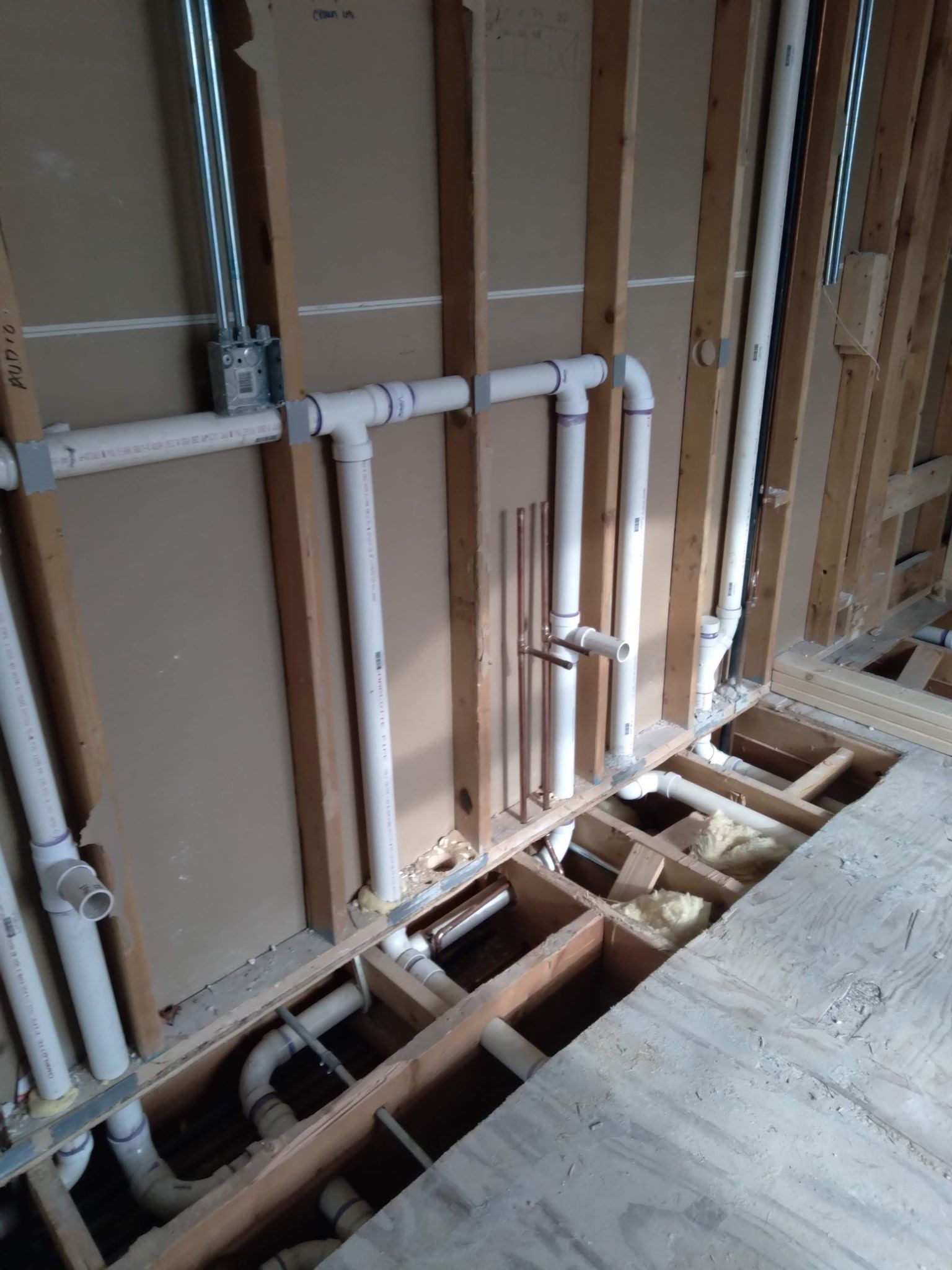 Exposed wall framing with white PVC plumbing pipes and open floor joists in a renovation area