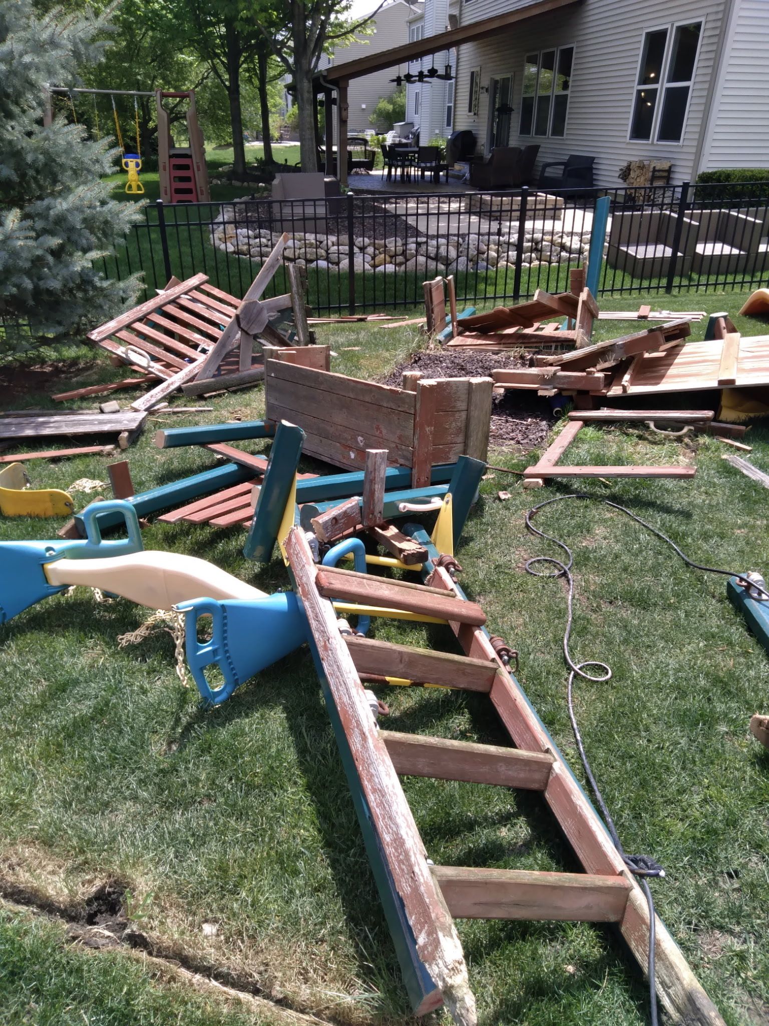 Broken playground equipment scattered on grass near a house and patio.