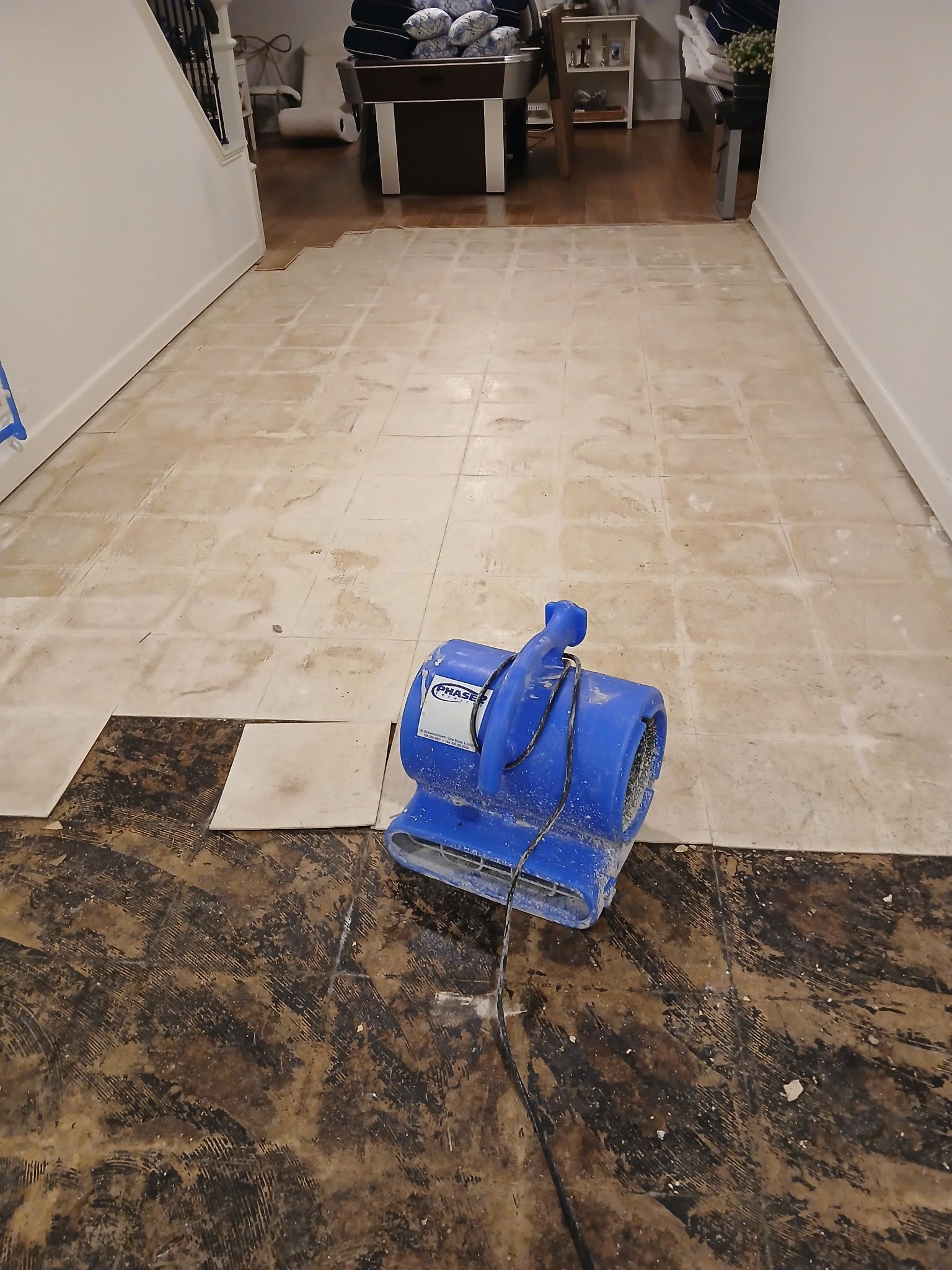 Blue floor-cleaning machine on a tiled hallway floor, with a dark wet area in the foreground.