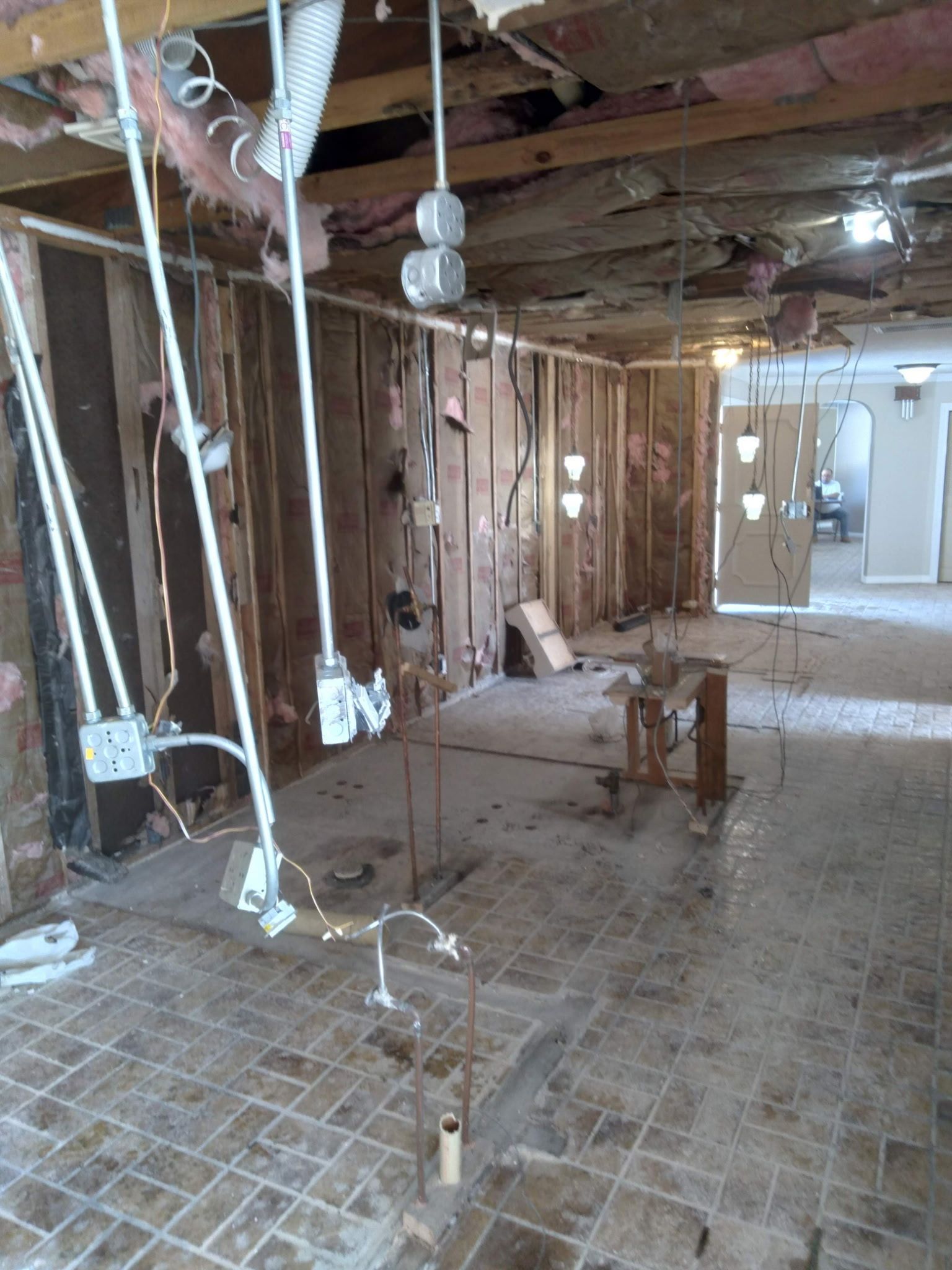 Damaged interior with exposed studs, hanging wires, debris, and a partially torn-down ceiling during renovation or demolition