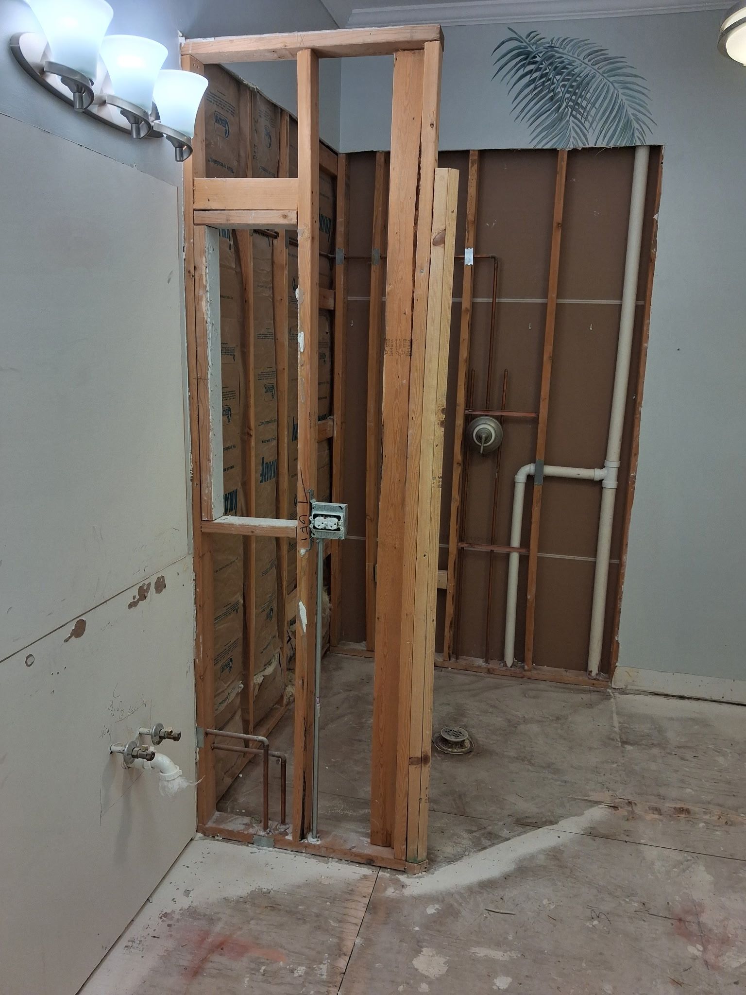 Exposed wooden wall framing in an unfinished interior room with plumbing pipes and construction debris on the floor