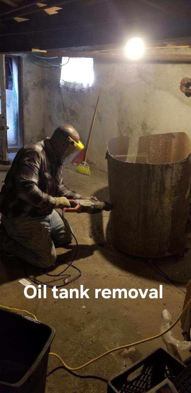 Worker in protective gear cleaning inside an oil tank with a pressure washer.
