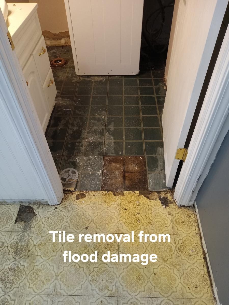 Damaged hallway tile being removed after flood, with exposed subfloor and debris