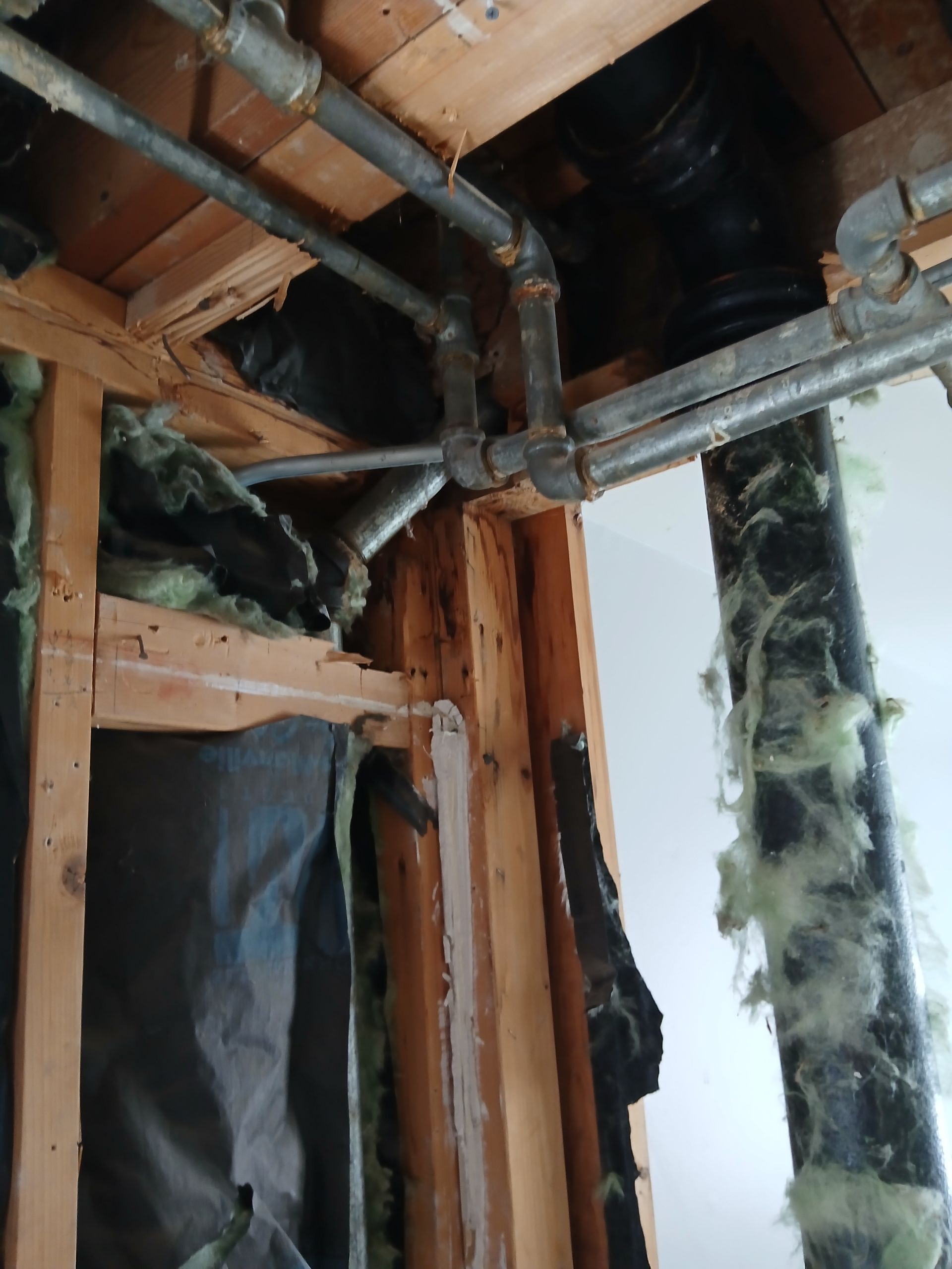 Partially demolished interior wall with exposed wood framing, metal pipes, and insulation around a window opening