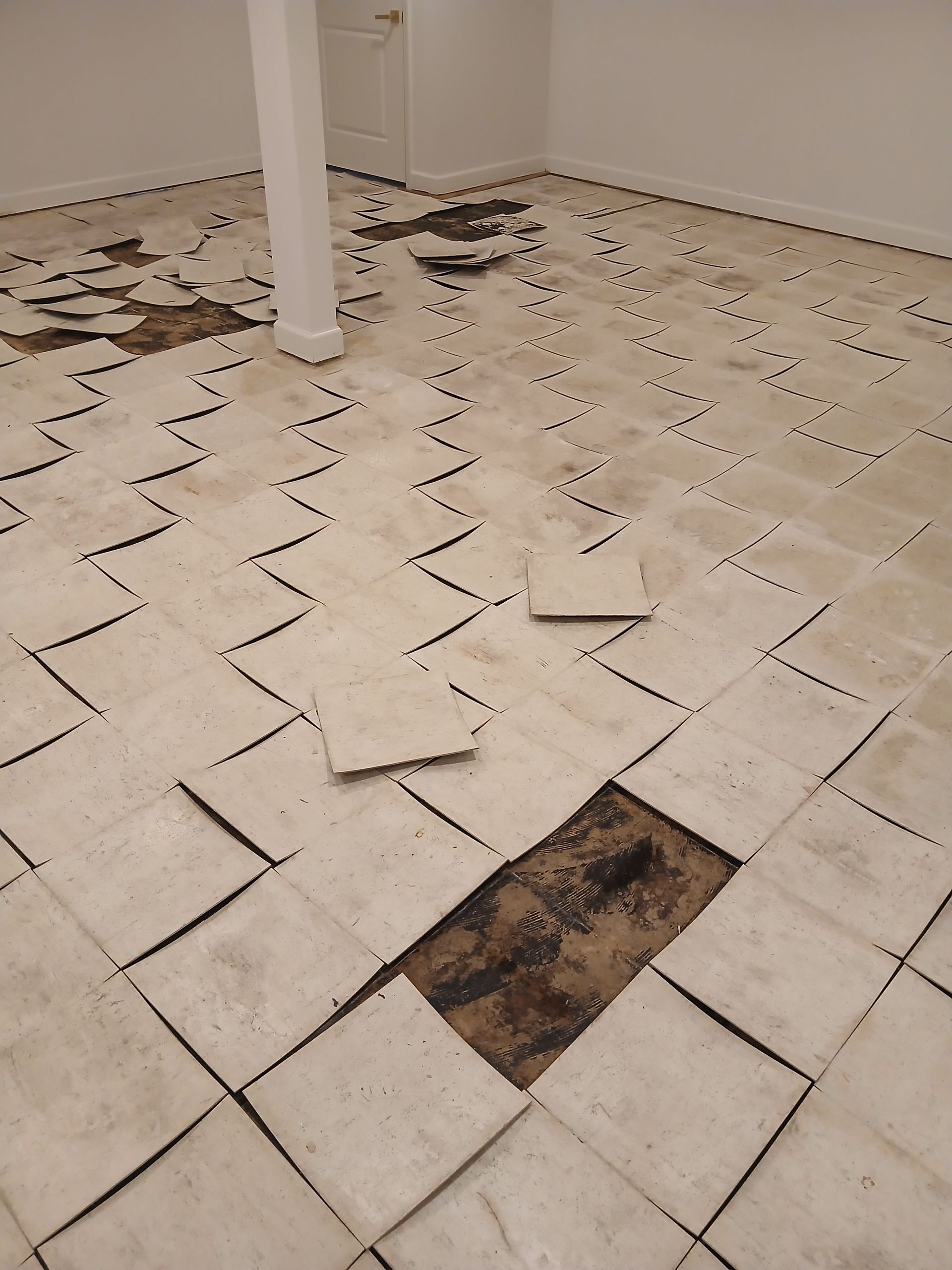 Damaged white tiled floor with several loose, lifted tiles and one exposed dark patch near a pillar.