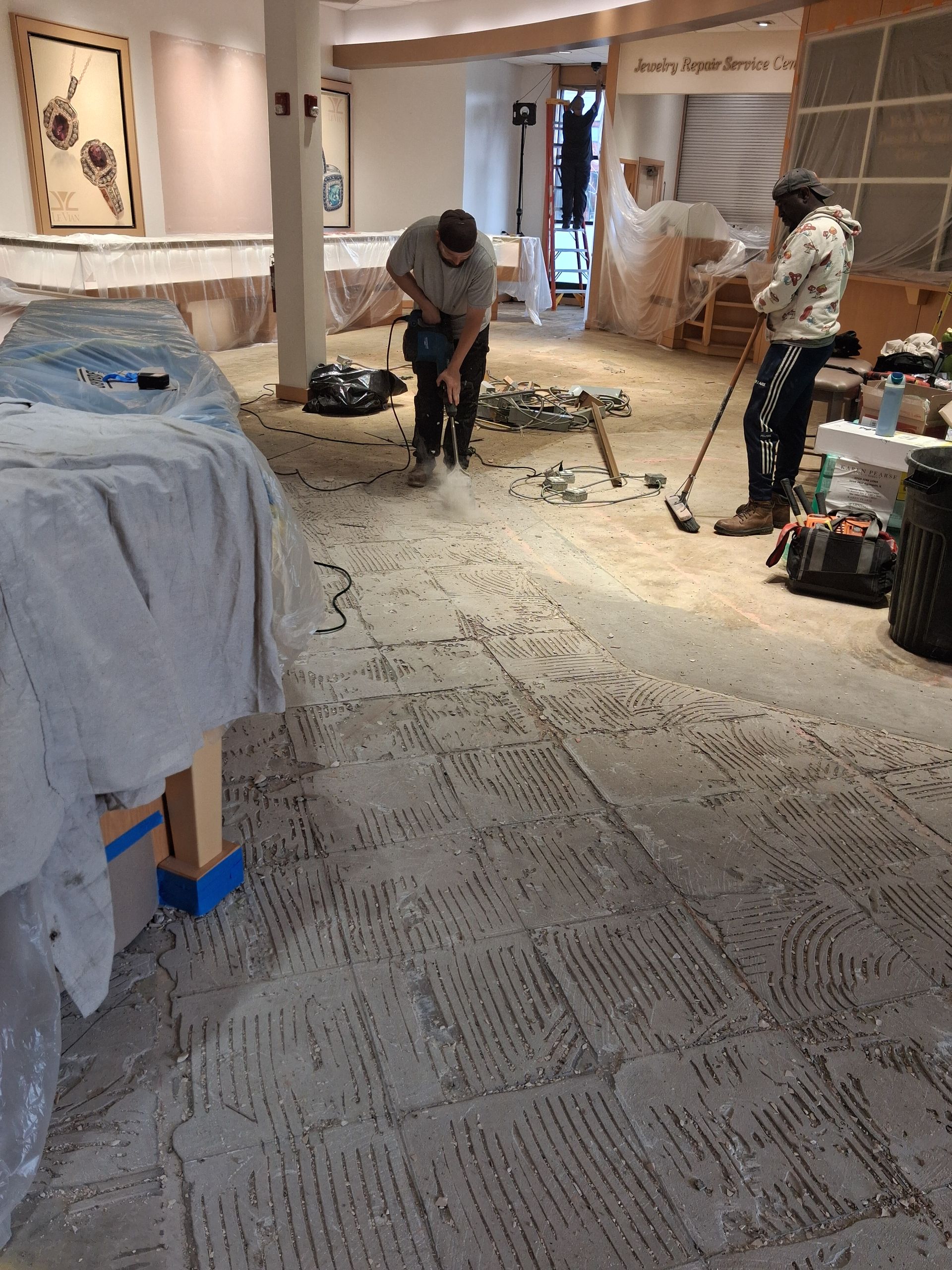 Workers vacuuming carpet in a hotel room under renovation, with furniture covered in dust sheets.