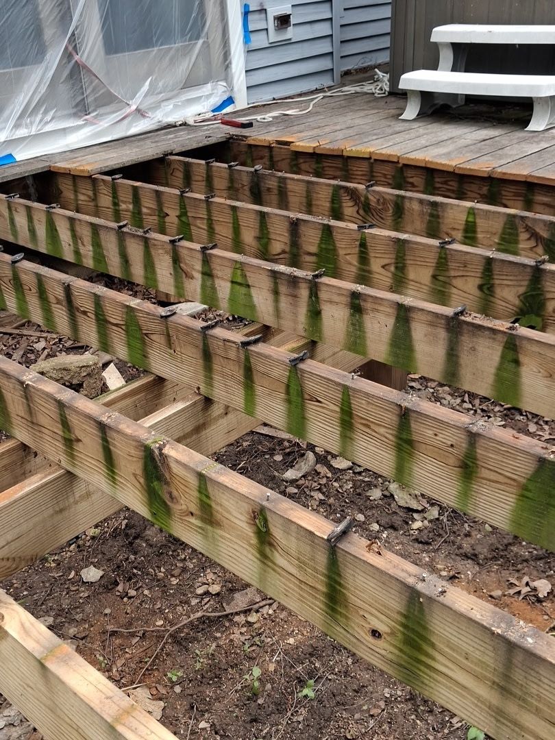 Wooden terraced retaining wall with moss stains beside a house deck and steps outdoors