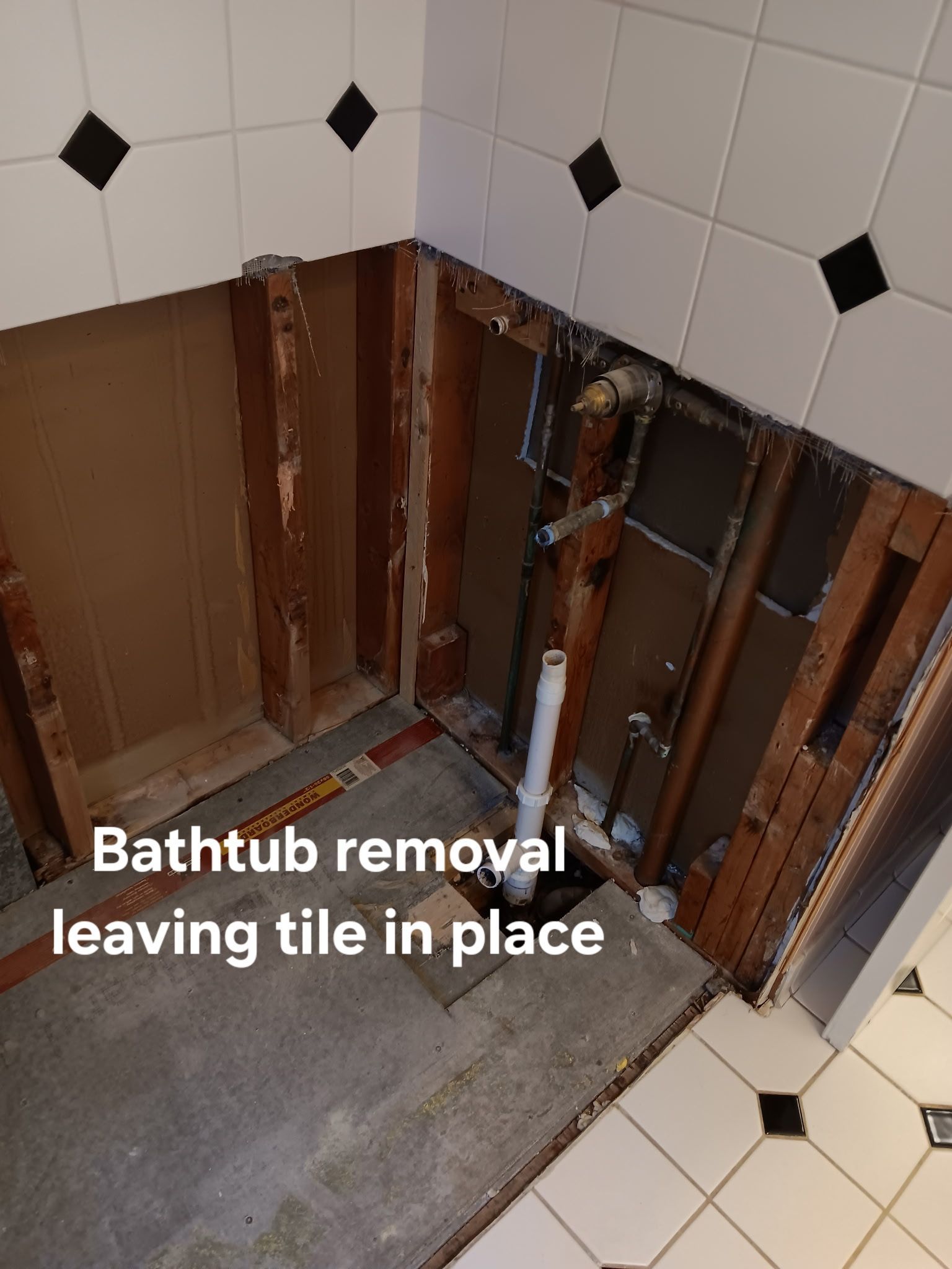 Bathtub removed, leaving exposed wall studs and tile in a bathroom renovation