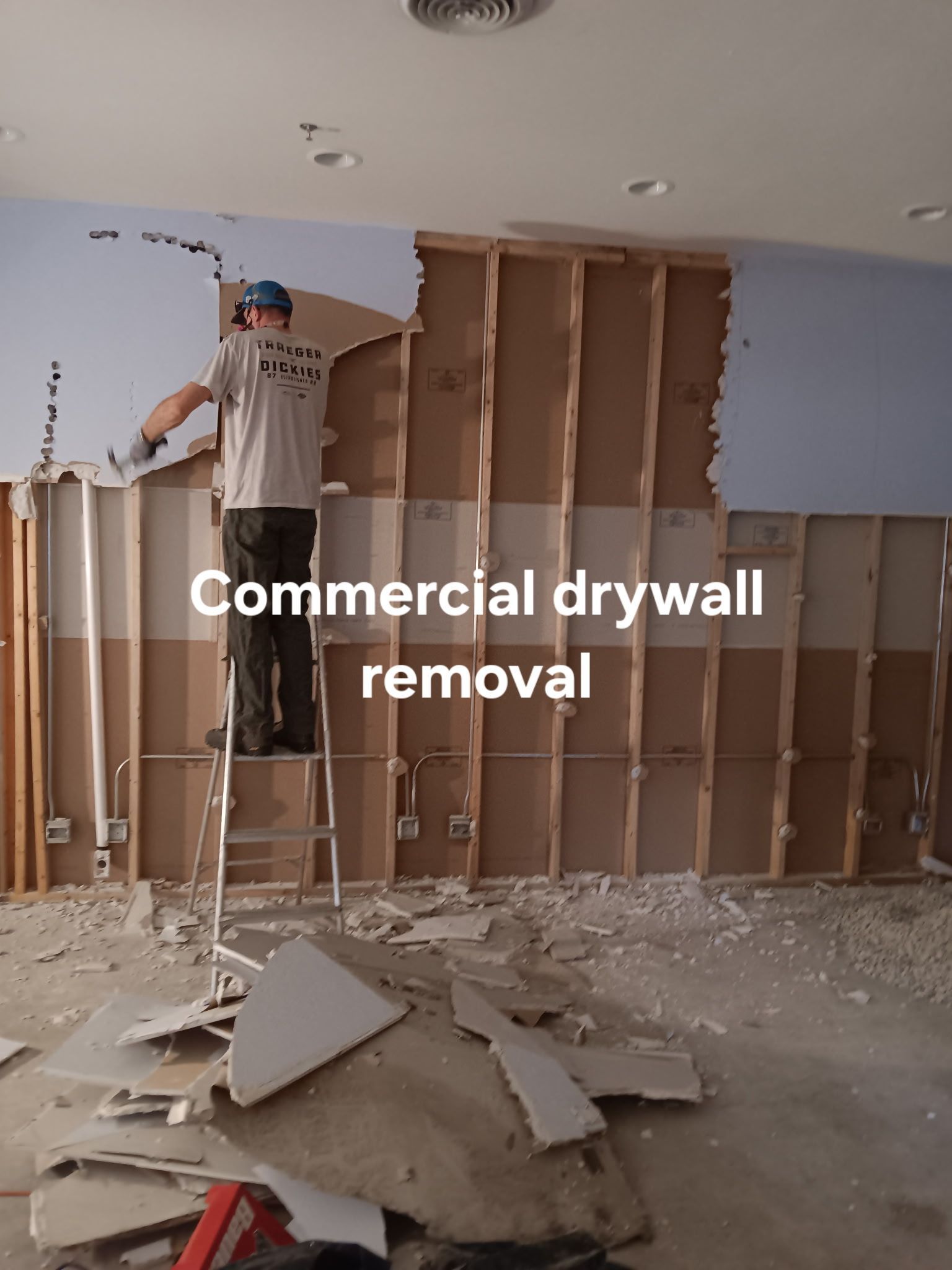 Commercial drywall removal in progress, with exposed studs and debris in an unfinished room