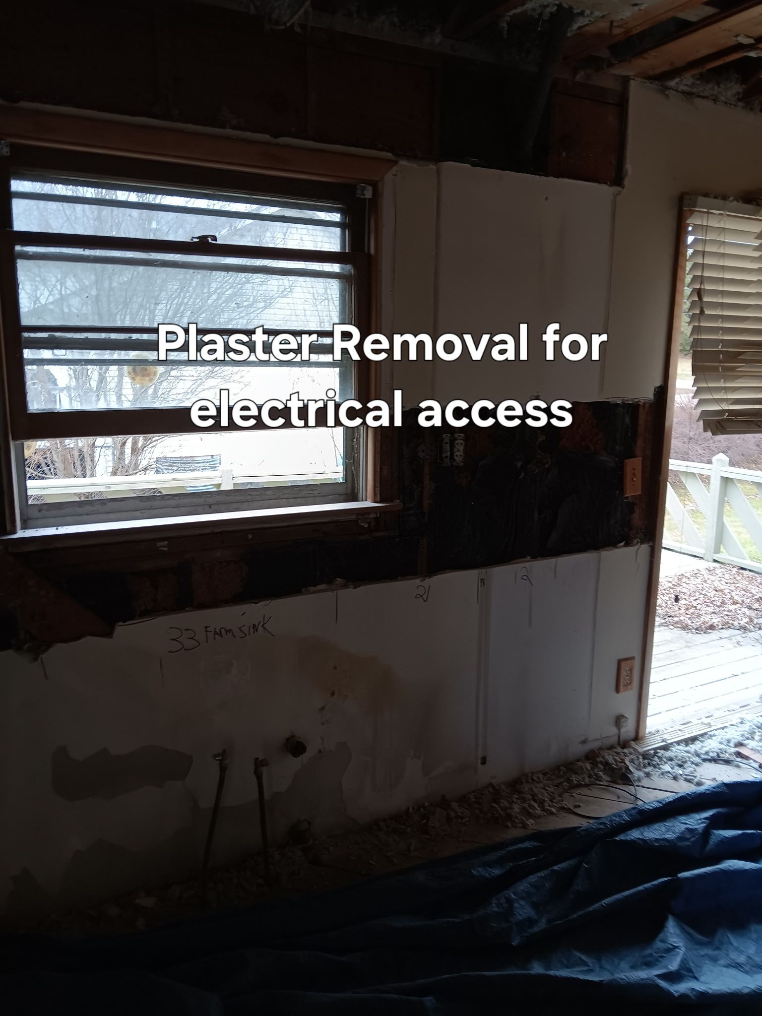 Room with stripped plaster for electrical access, showing a window and exposed wall framing.