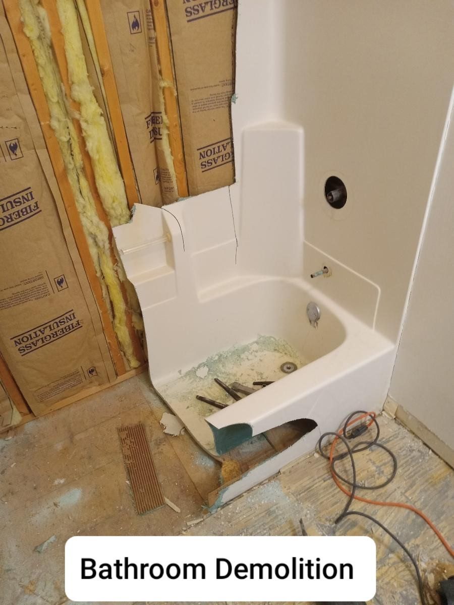 Bathroom under demolition with exposed insulation, torn drywall, and a damaged tub surround.
