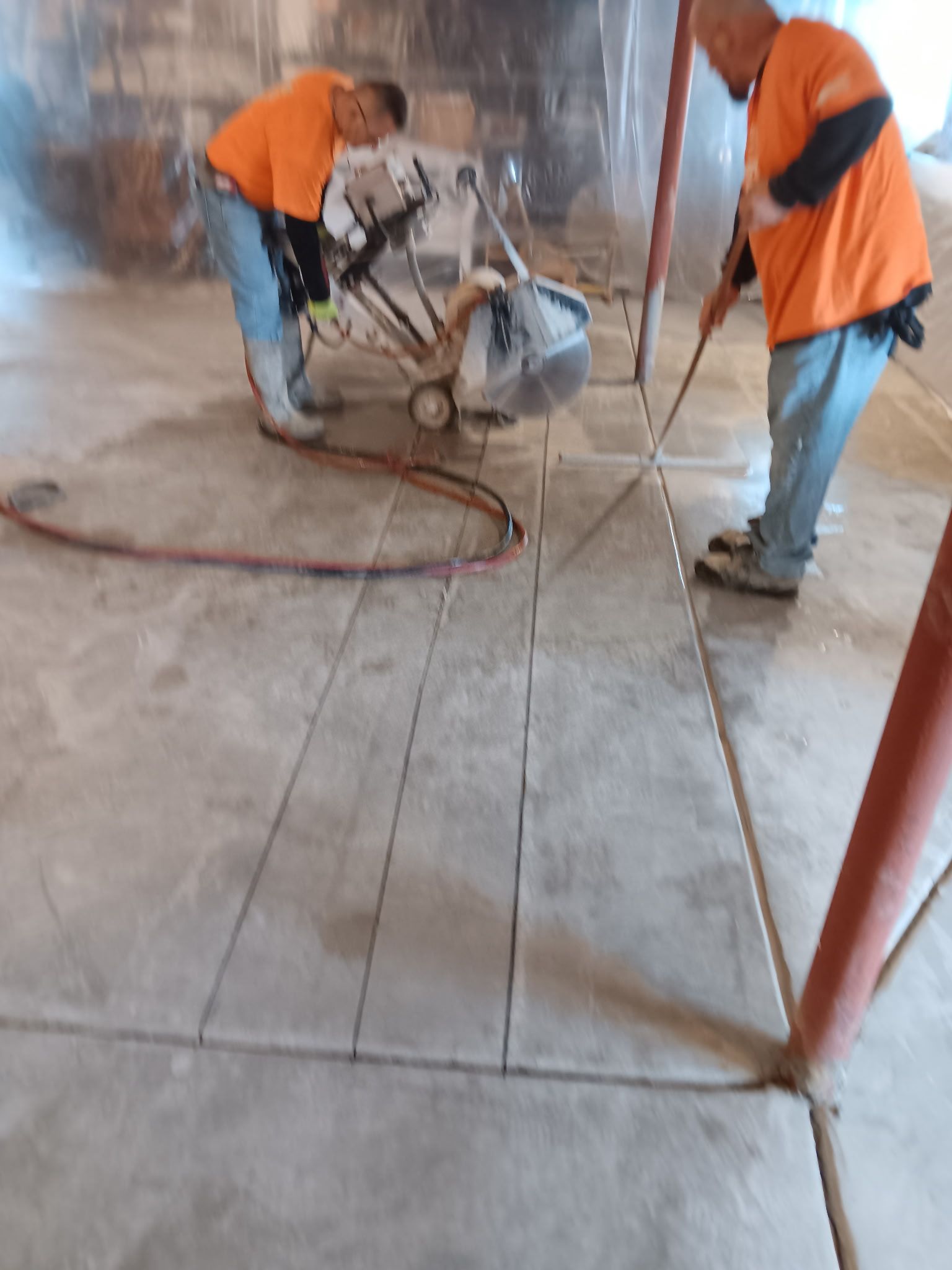 Workers using a floor grinder on a dusty concrete floor indoors