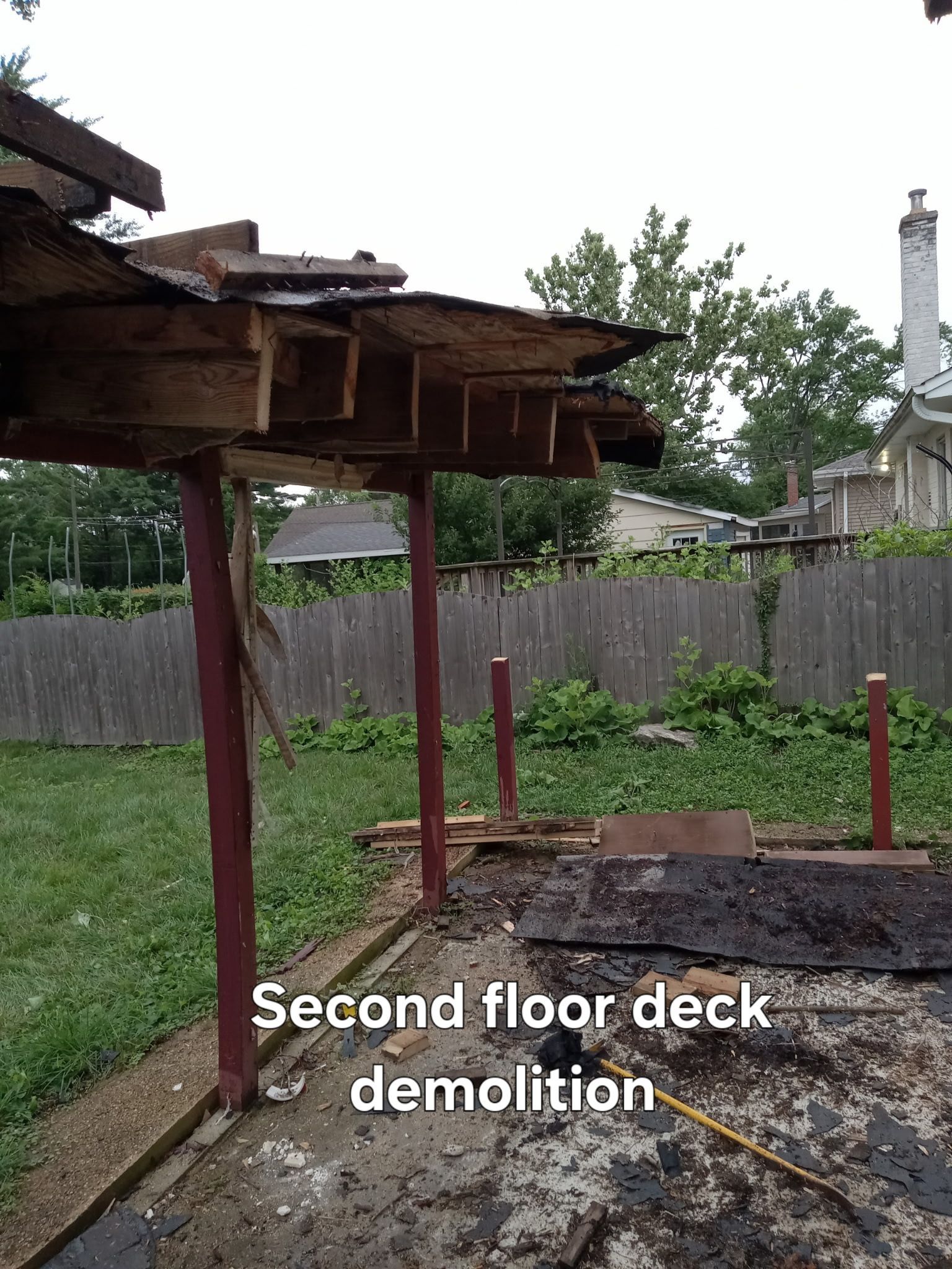 Second-floor deck demolition with exposed beams and posts in a backyard
