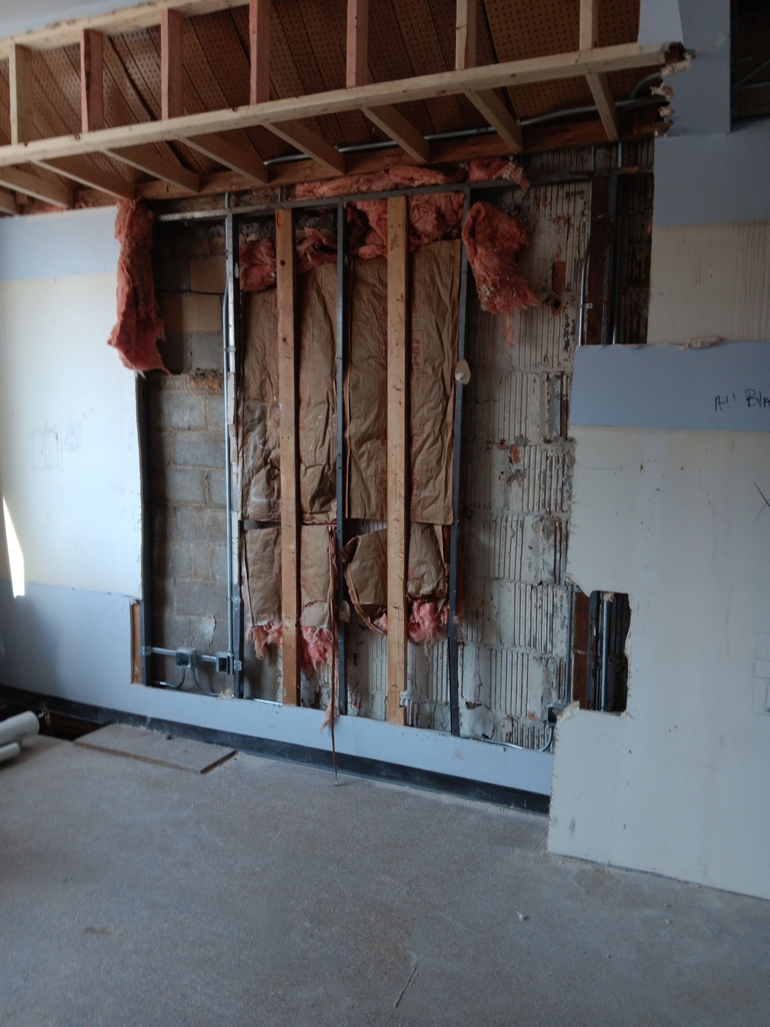 Exposed wall framing and insulation in an unfinished room with drywall removed.