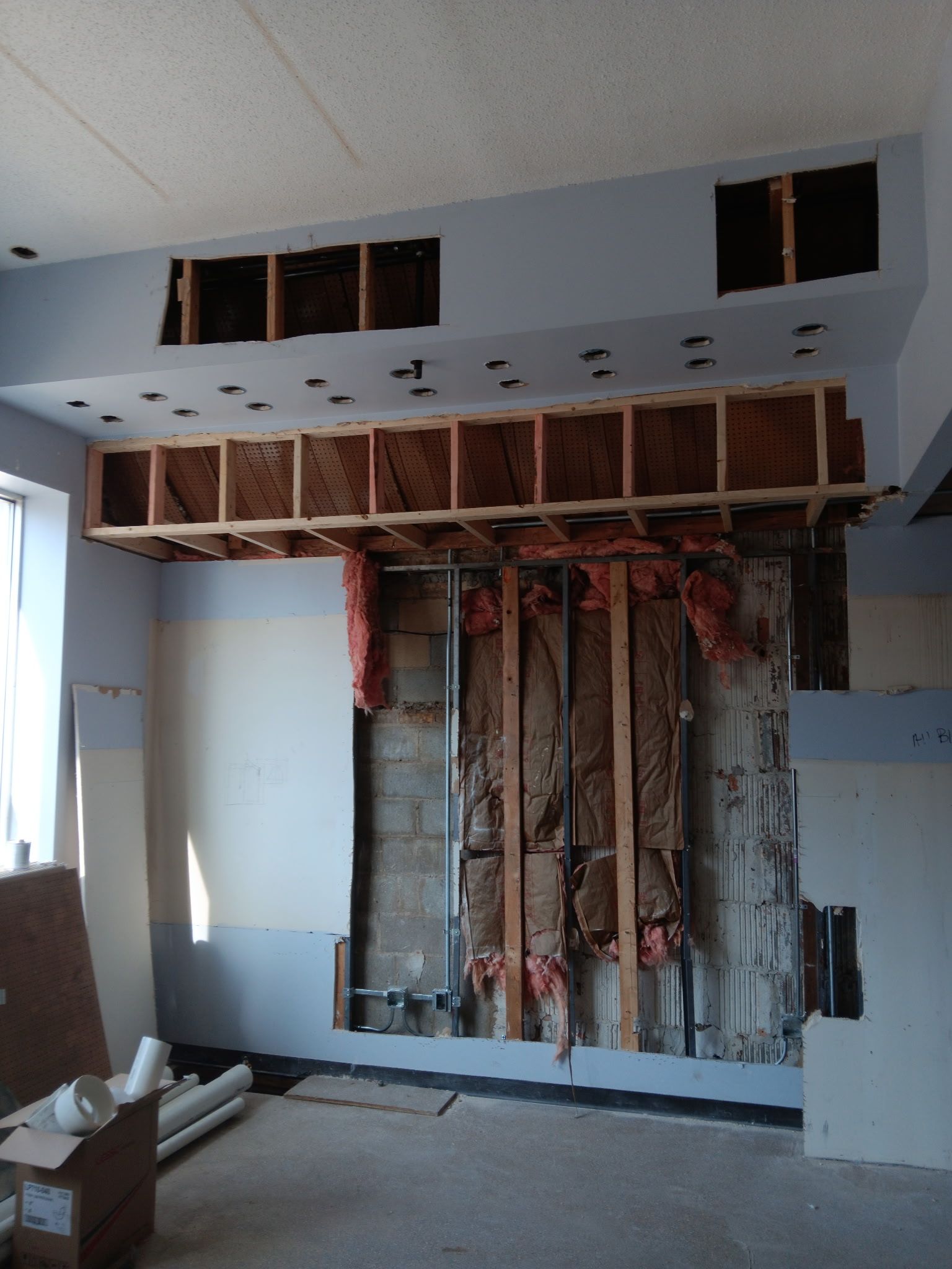 Partially demolished interior wall with exposed studs, drywall, and wiring in a room under renovation