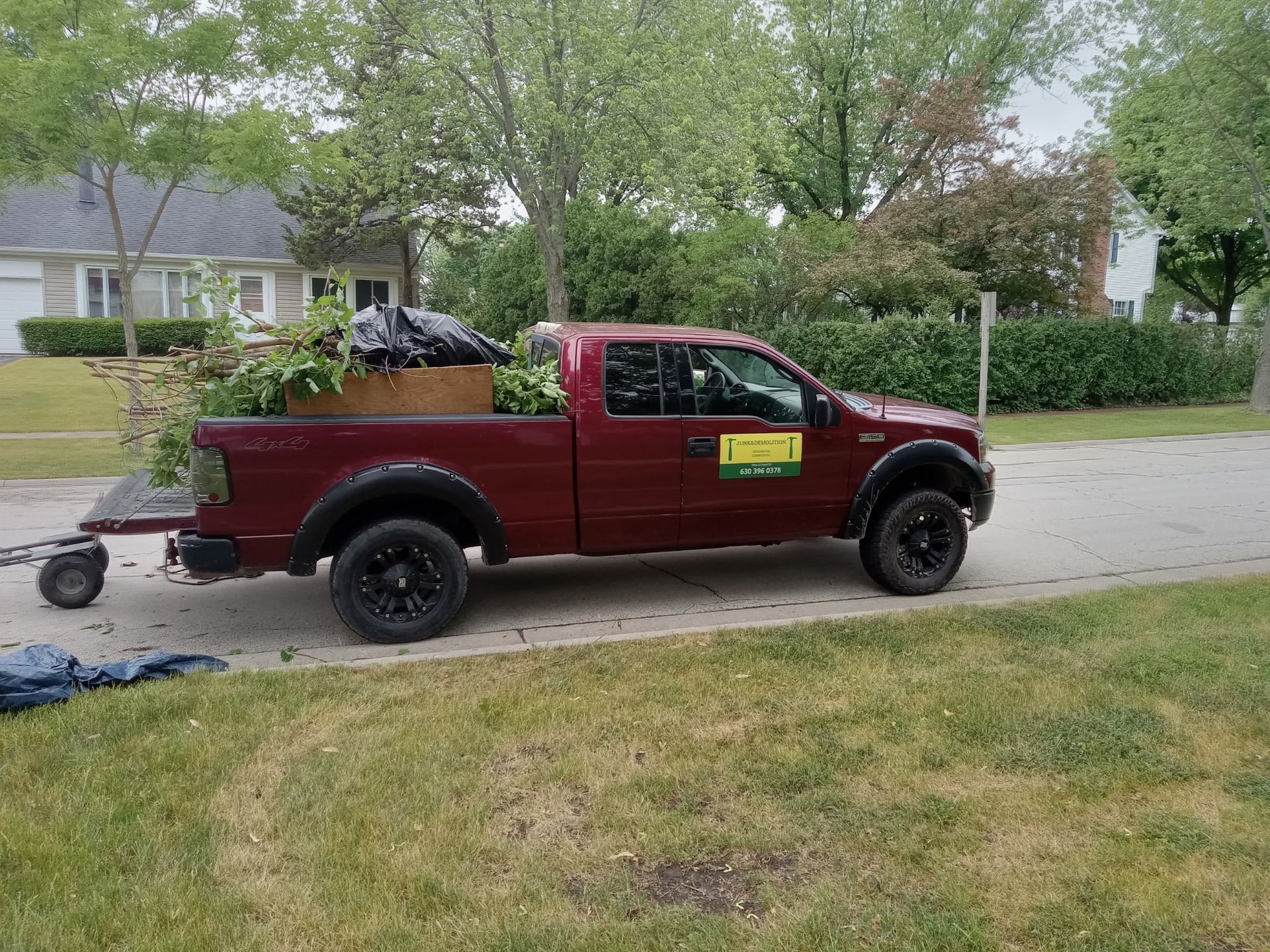 Red pickup truck parked on a residential street beside a grassy lawn and trees.