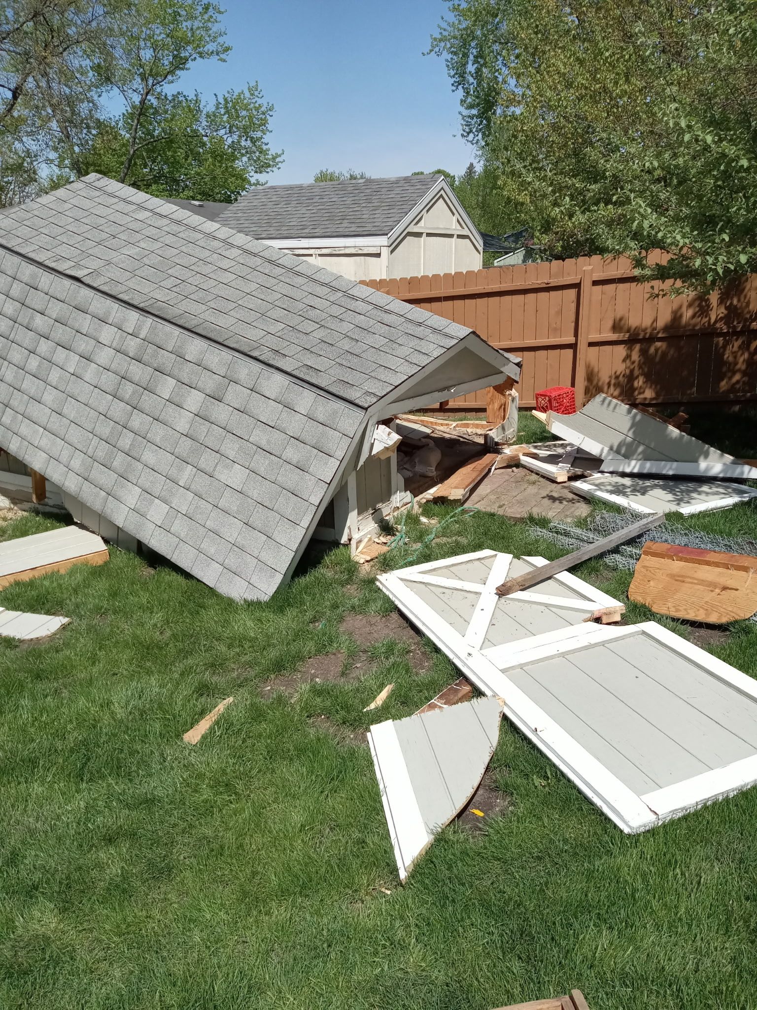 Collapsed fence panels and debris scattered across a backyard lawn after storm damage.