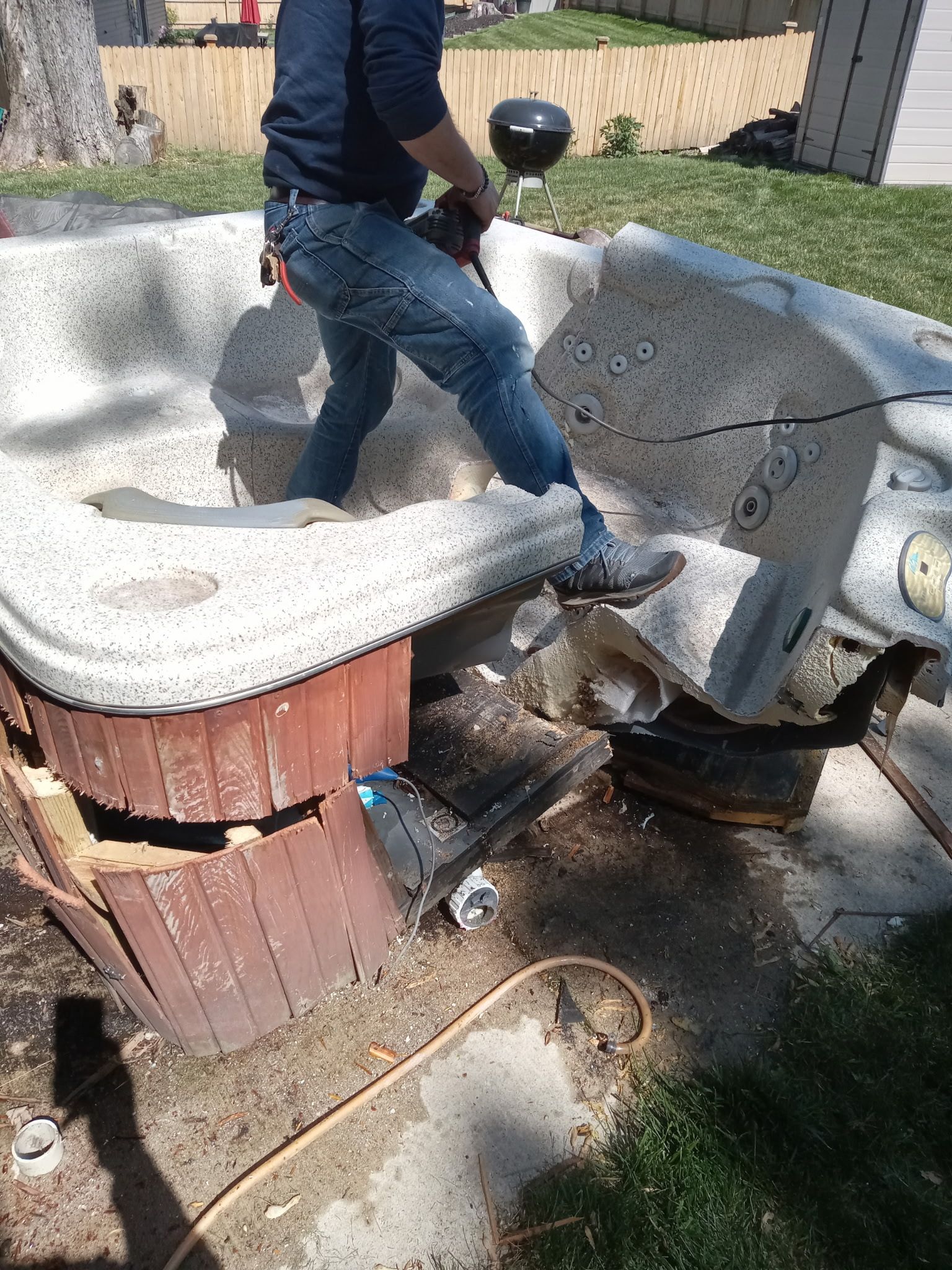 Person standing on a damaged concrete structure beside a broken wooden fire pit in a yard