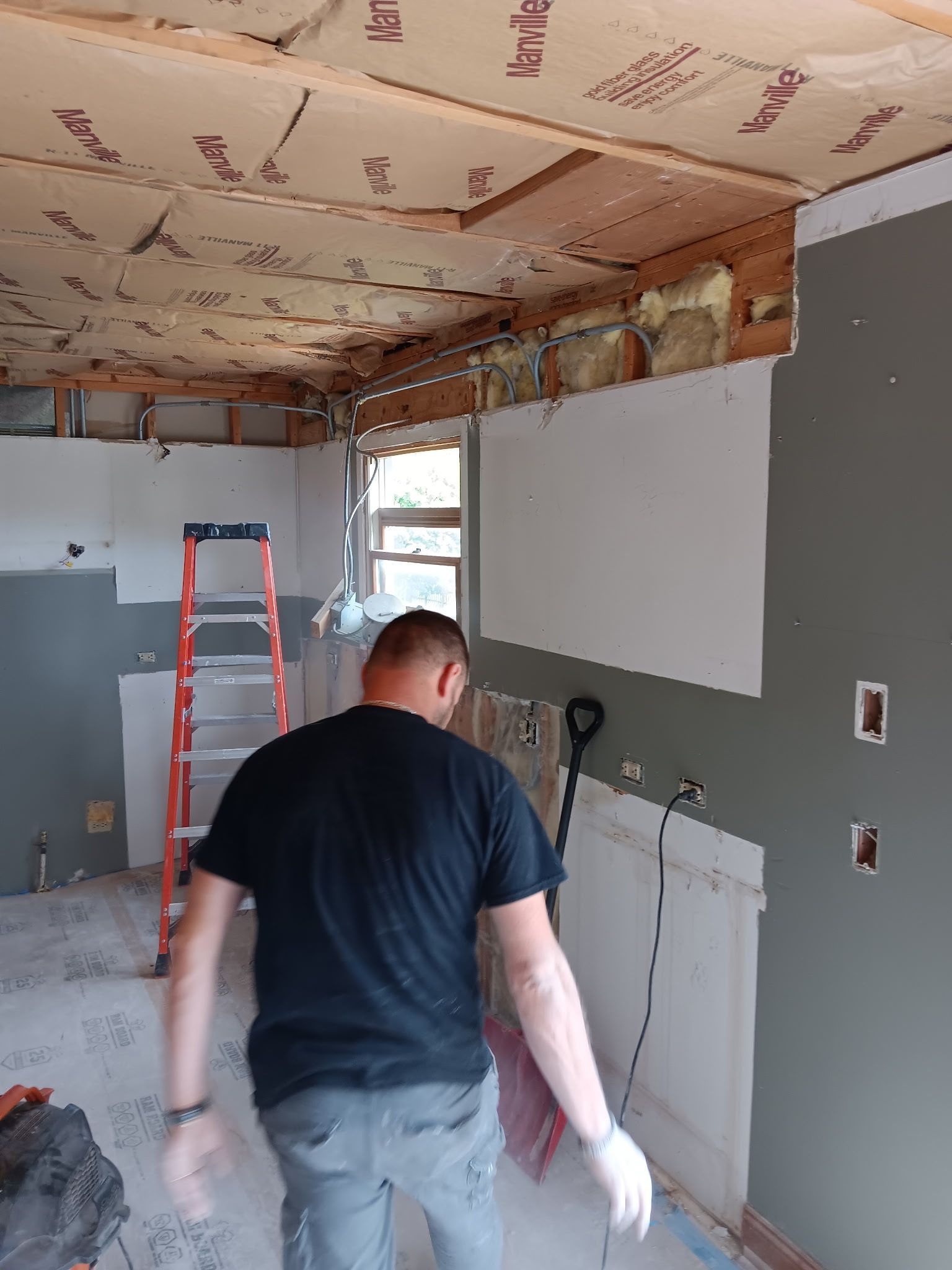 Person working in a partially renovated room with exposed ceiling and a ladder in the background