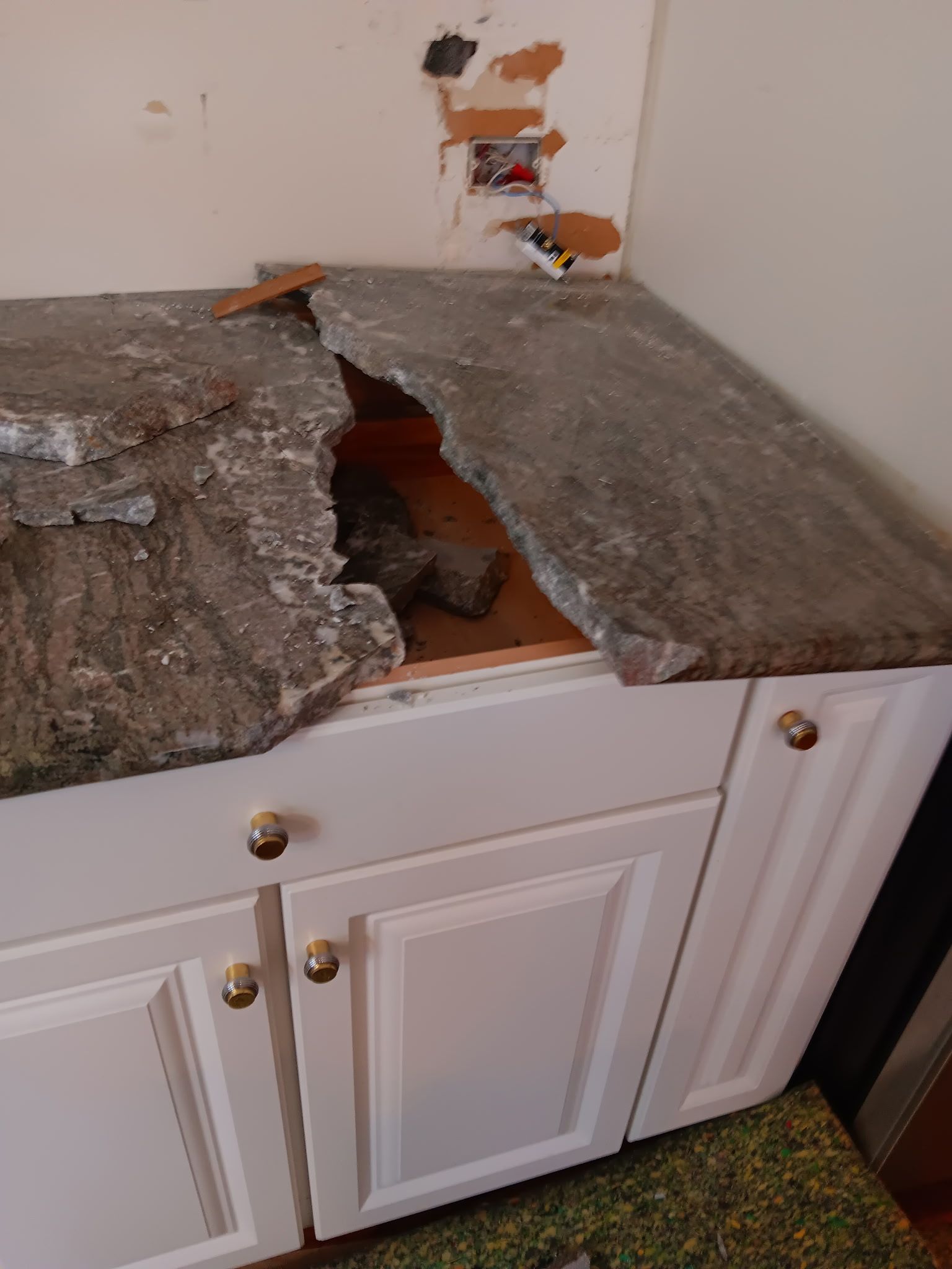 Broken countertop with a large hole above white cabinets in a kitchen area