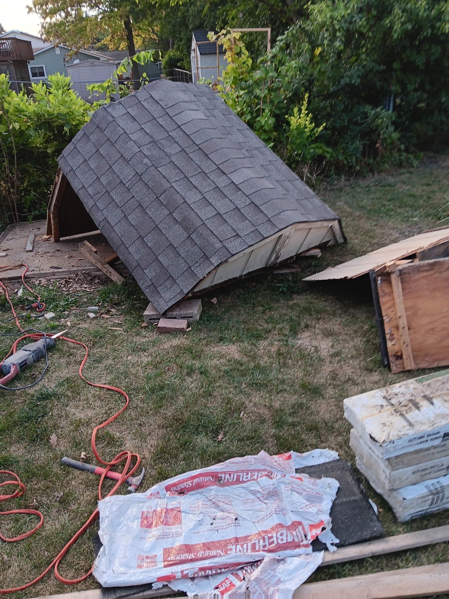 Collapsed shed roof in a yard with scattered construction materials and extension cords