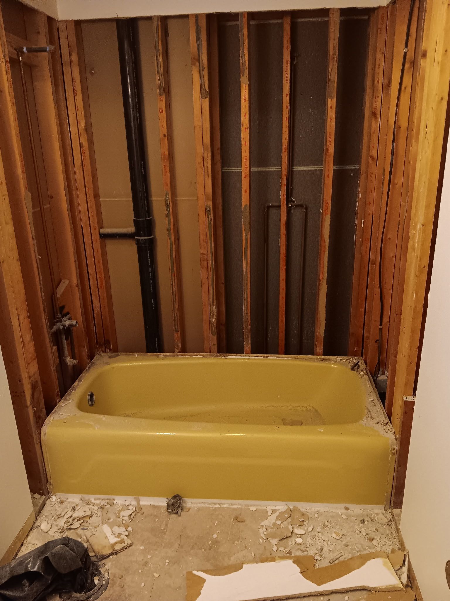 Bathroom with a yellow bathtub and exposed wall studs behind it during renovation