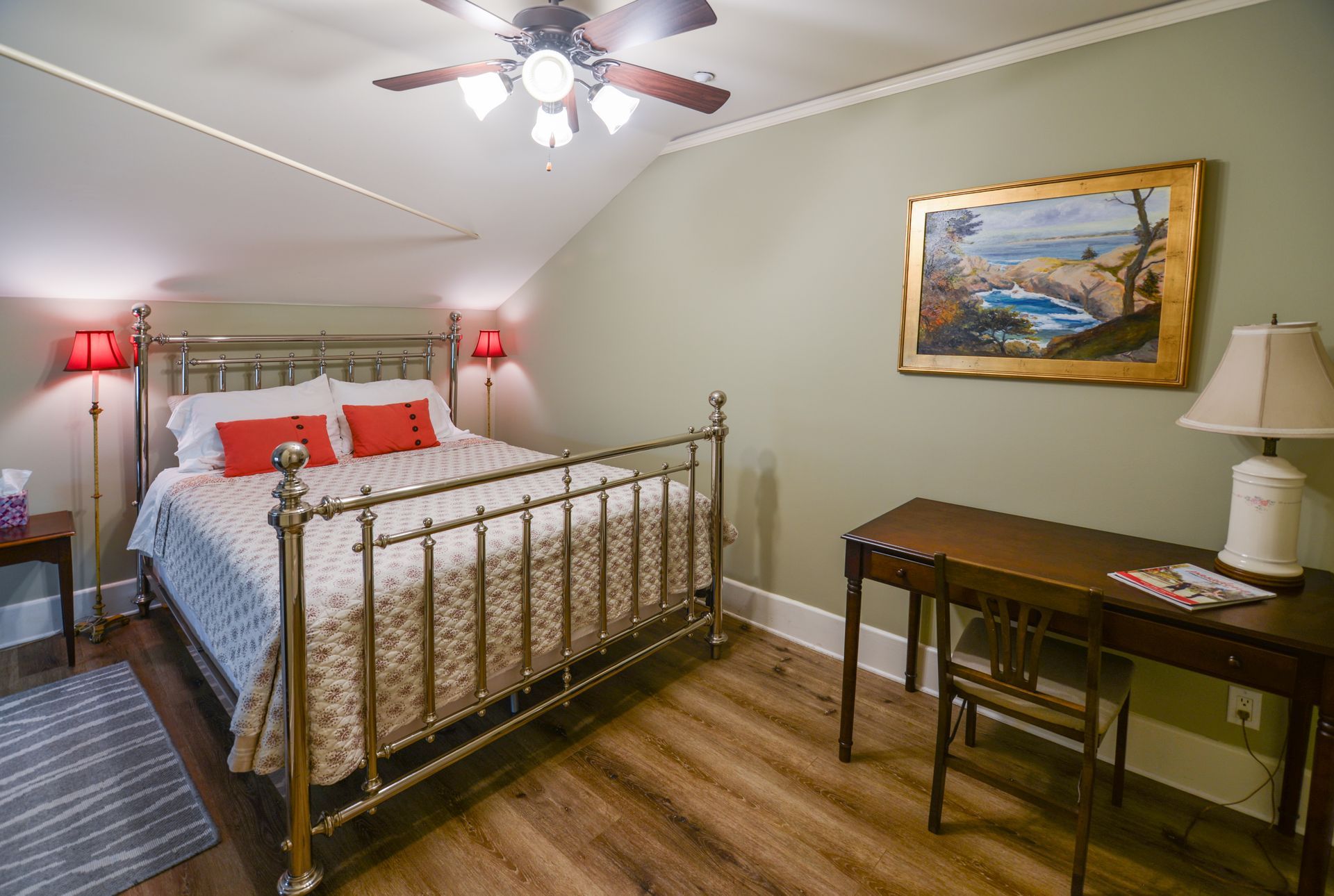 A bedroom with a bed , desk , lamp and ceiling fan.