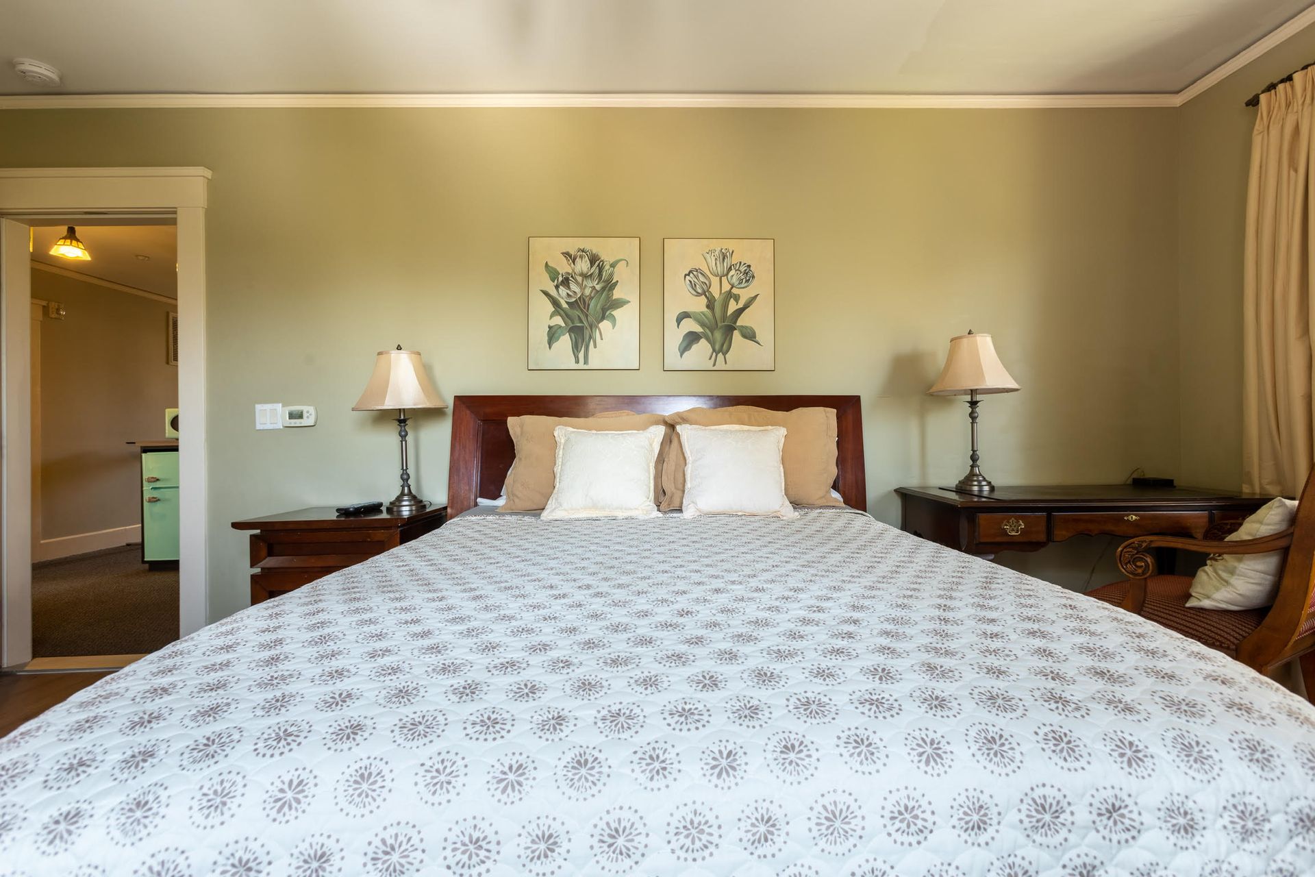 A bedroom with a king size bed , two nightstands , two lamps , and two paintings on the wall.