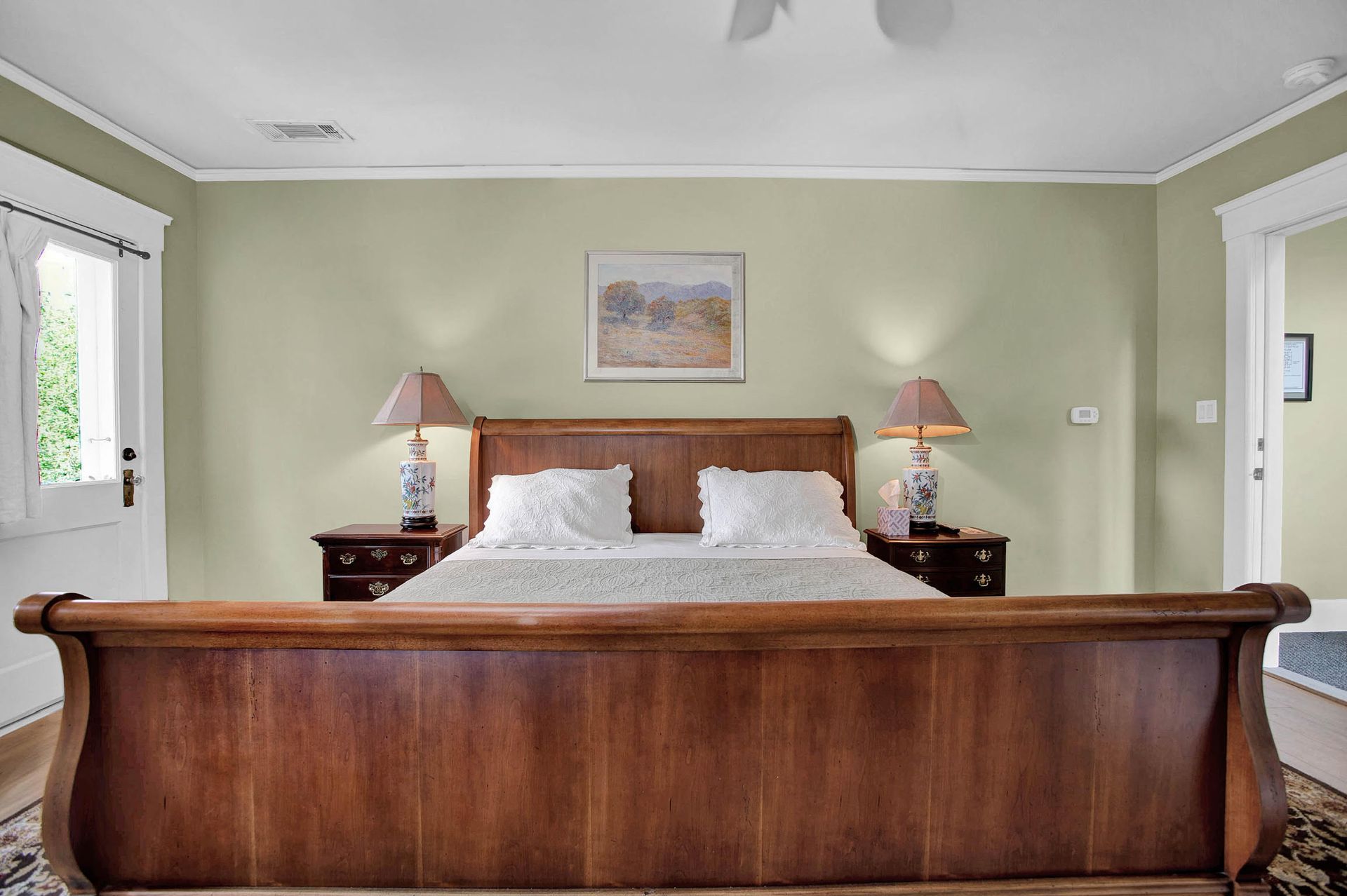 A bedroom with a king size bed , two nightstands , two lamps and a picture on the wall.
