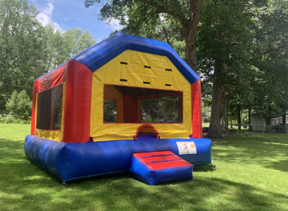 A red , yellow and blue bouncy house is sitting on top of a lush green field.