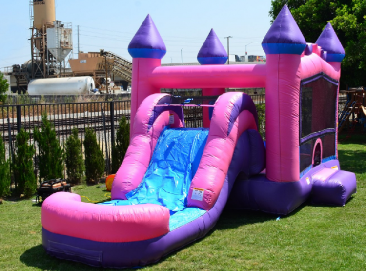 A pink and purple bouncy castle with a water slide