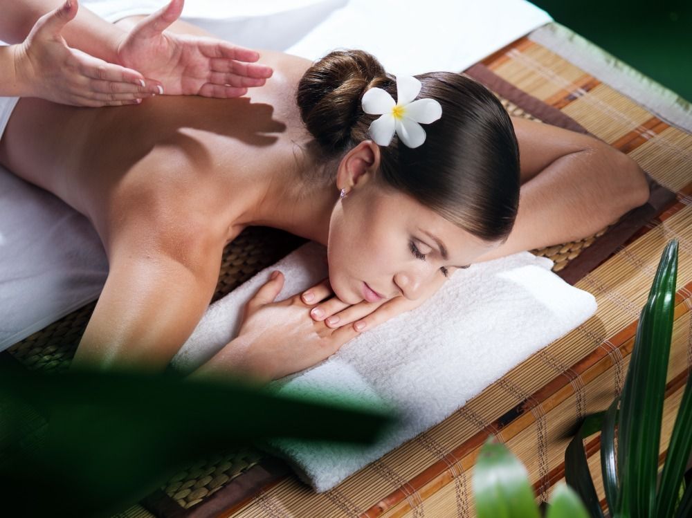Woman receiving a back massage on a spa table, with a white flower in her hair