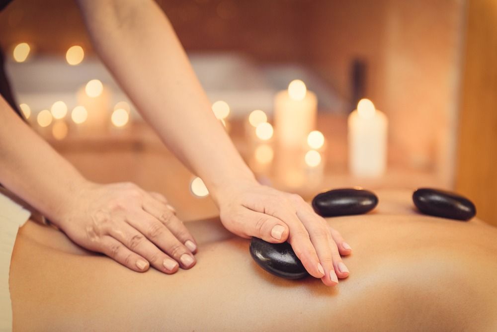 Massage therapist using hot stones on a client's back in a candlelit spa room