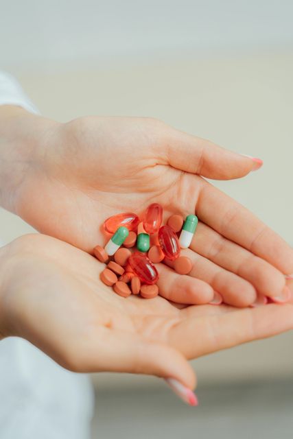 Mani che reggono capsule e compresse di vari colori: rosse, verdi e marroni.