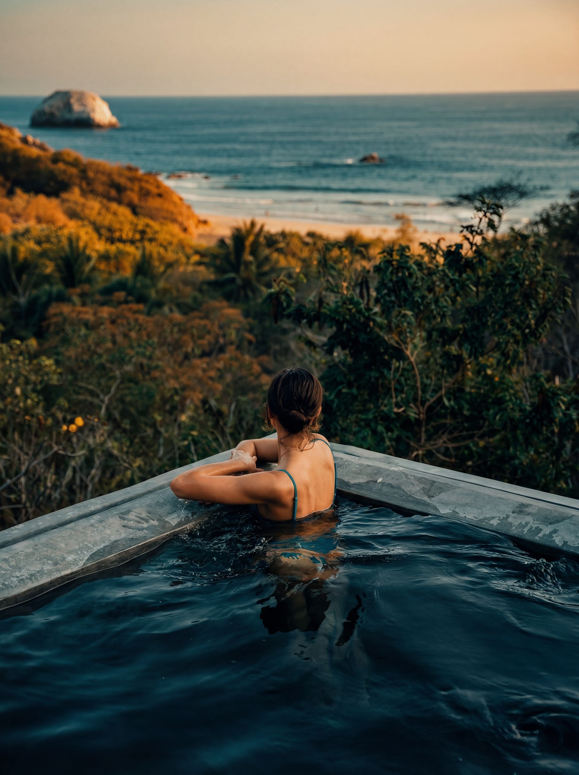 Person relaxing in a dark infinity pool overlooking the ocean at sunset