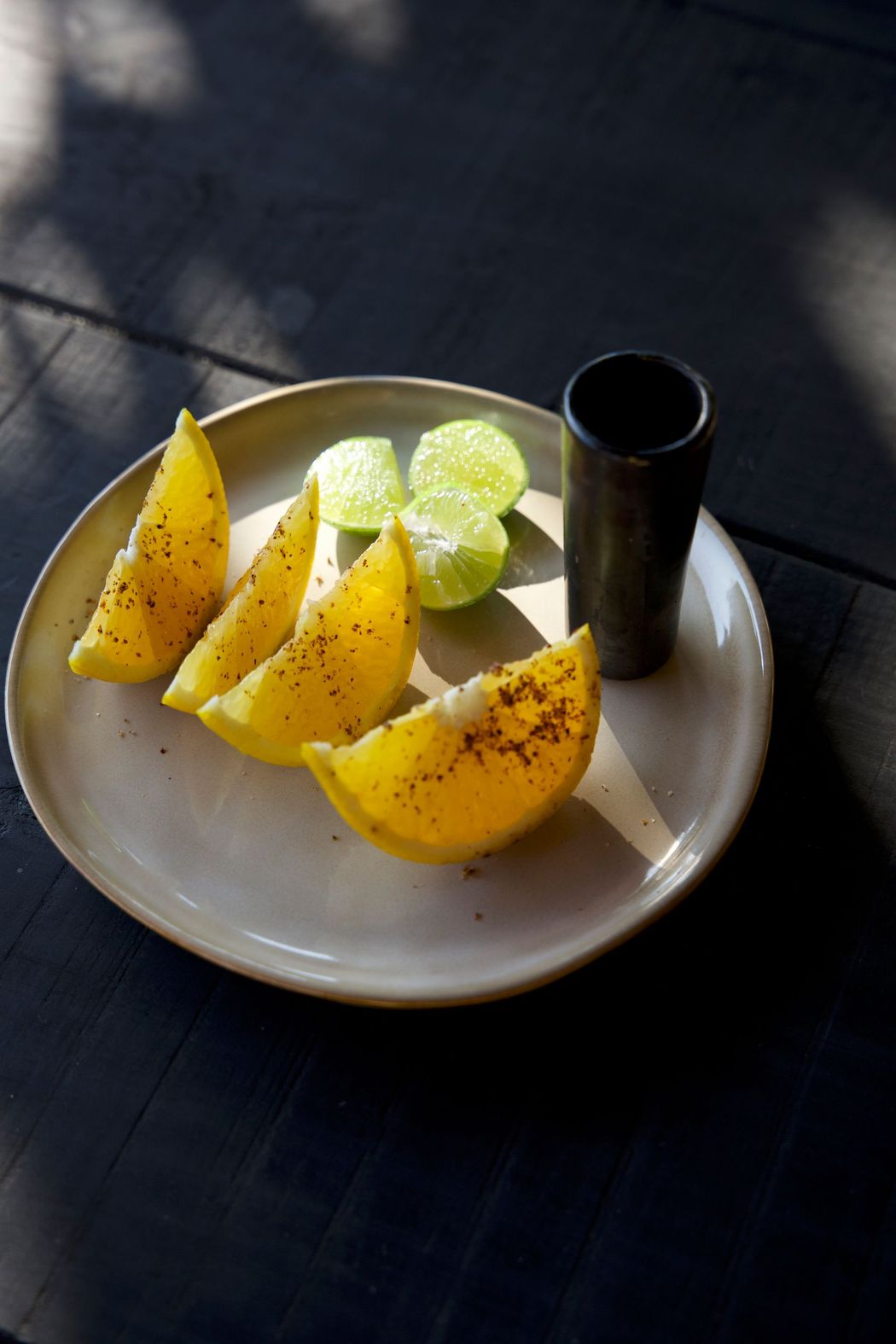 Plate with lemon wedges and a small black cup on a dark table in sunlight