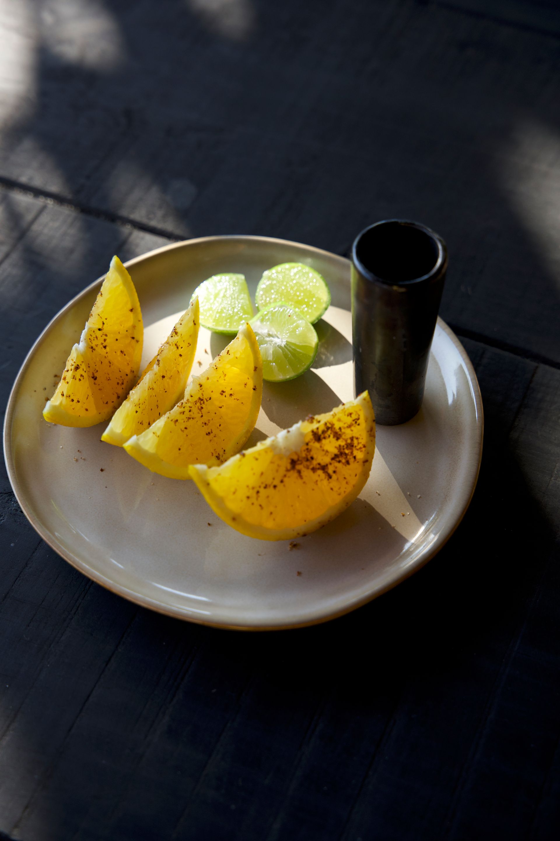 Plate with lemon wedges and a small black cup on a dark table in sunlight