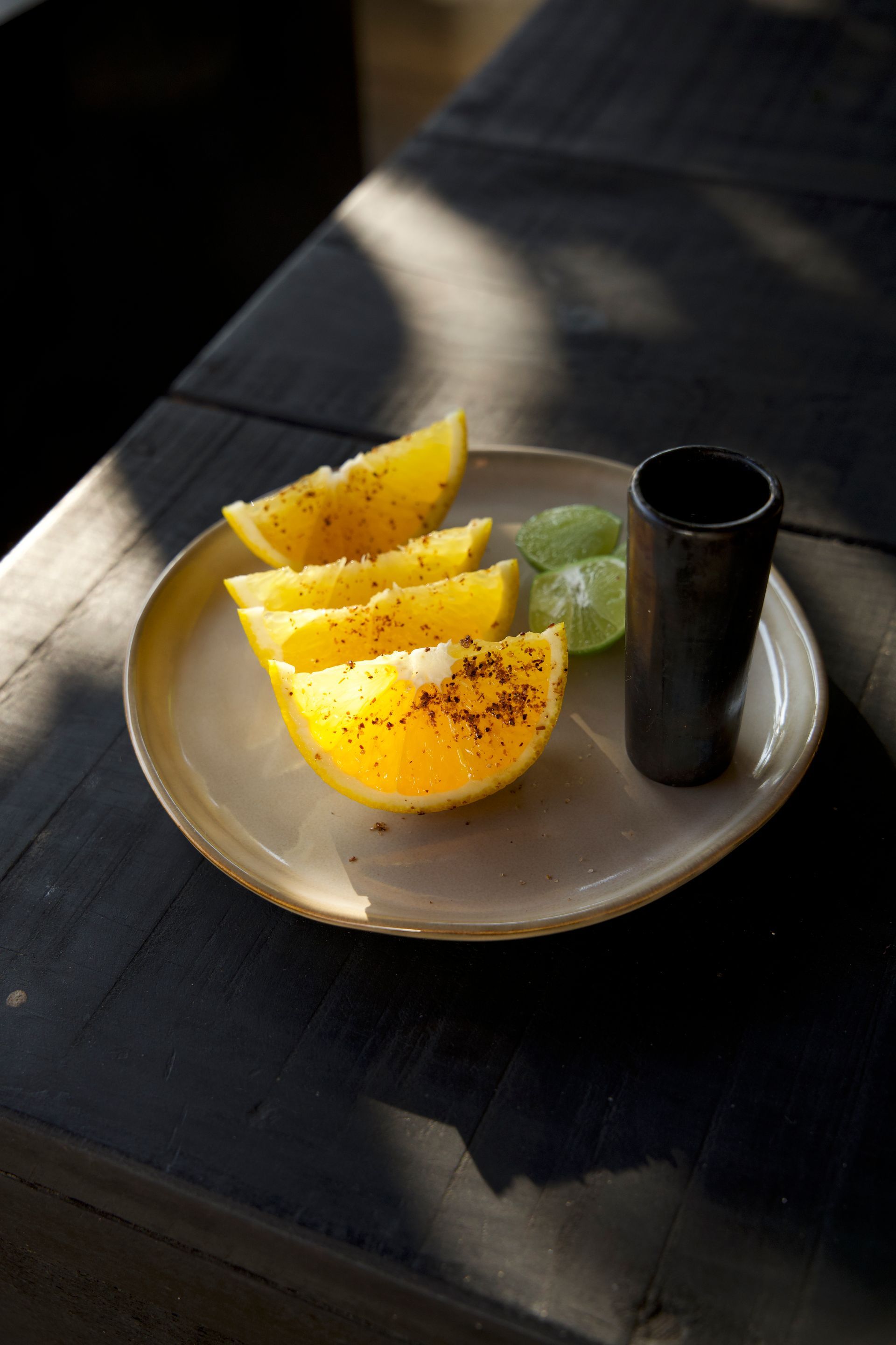 Sliced yellow fruit on a plate with a green garnish and a black cup on a sunlit table